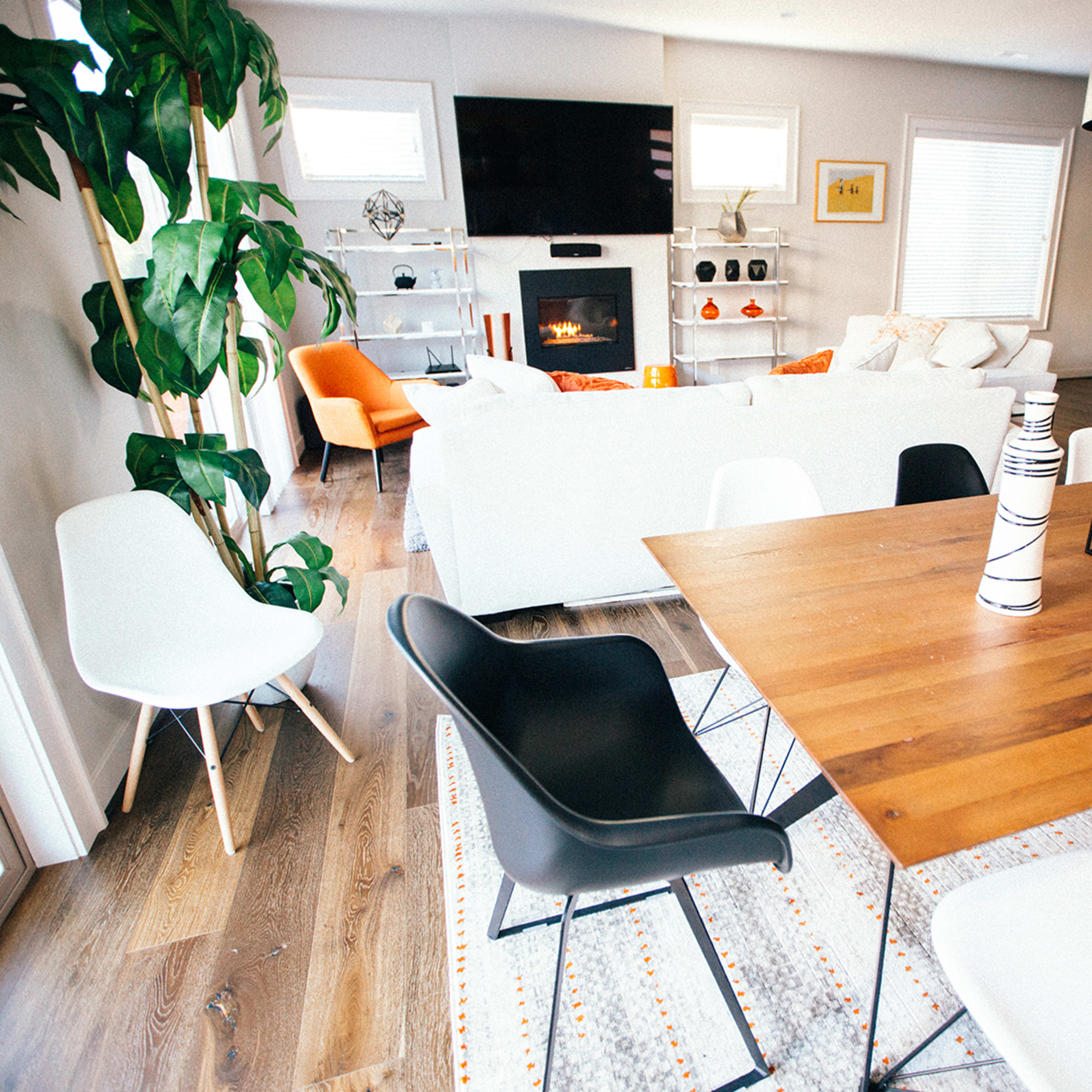 A modern living space with a dining table surrounded by various chairs, a white sofa in the background, and a large television mounted on the wall.