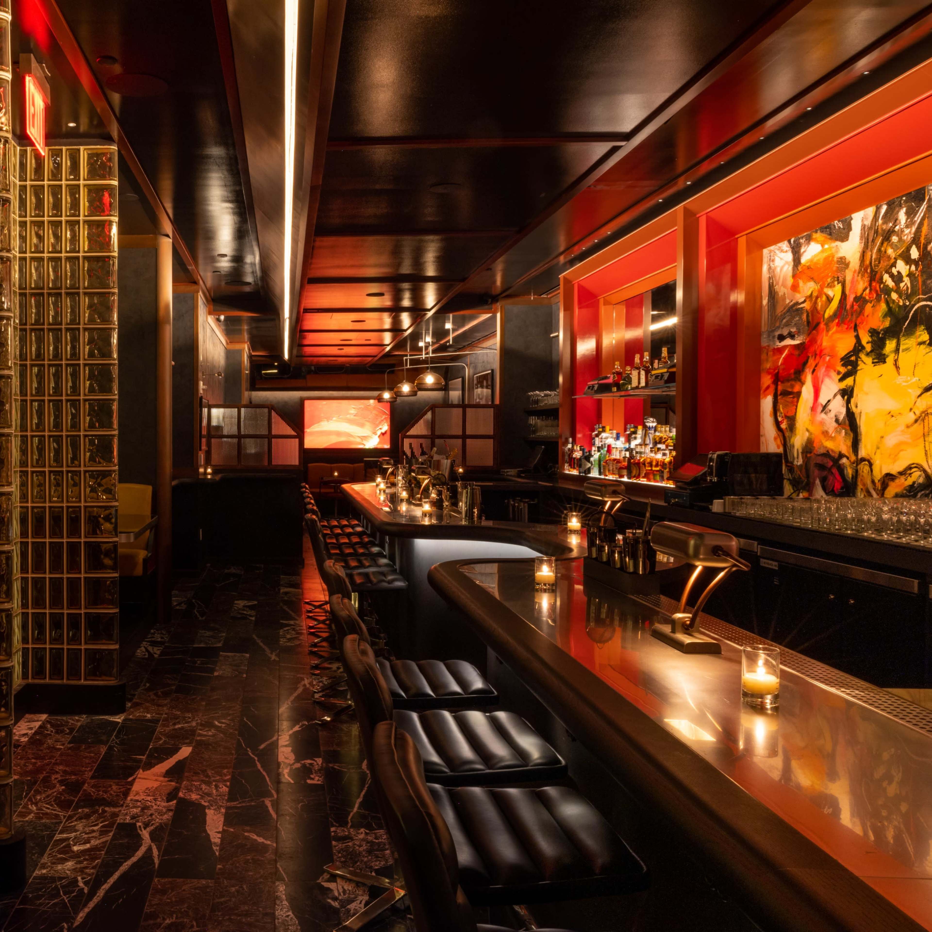A modern bar interior with a sleek black and gold design, featuring a long bar, seating areas, and illuminated glass block walls.
