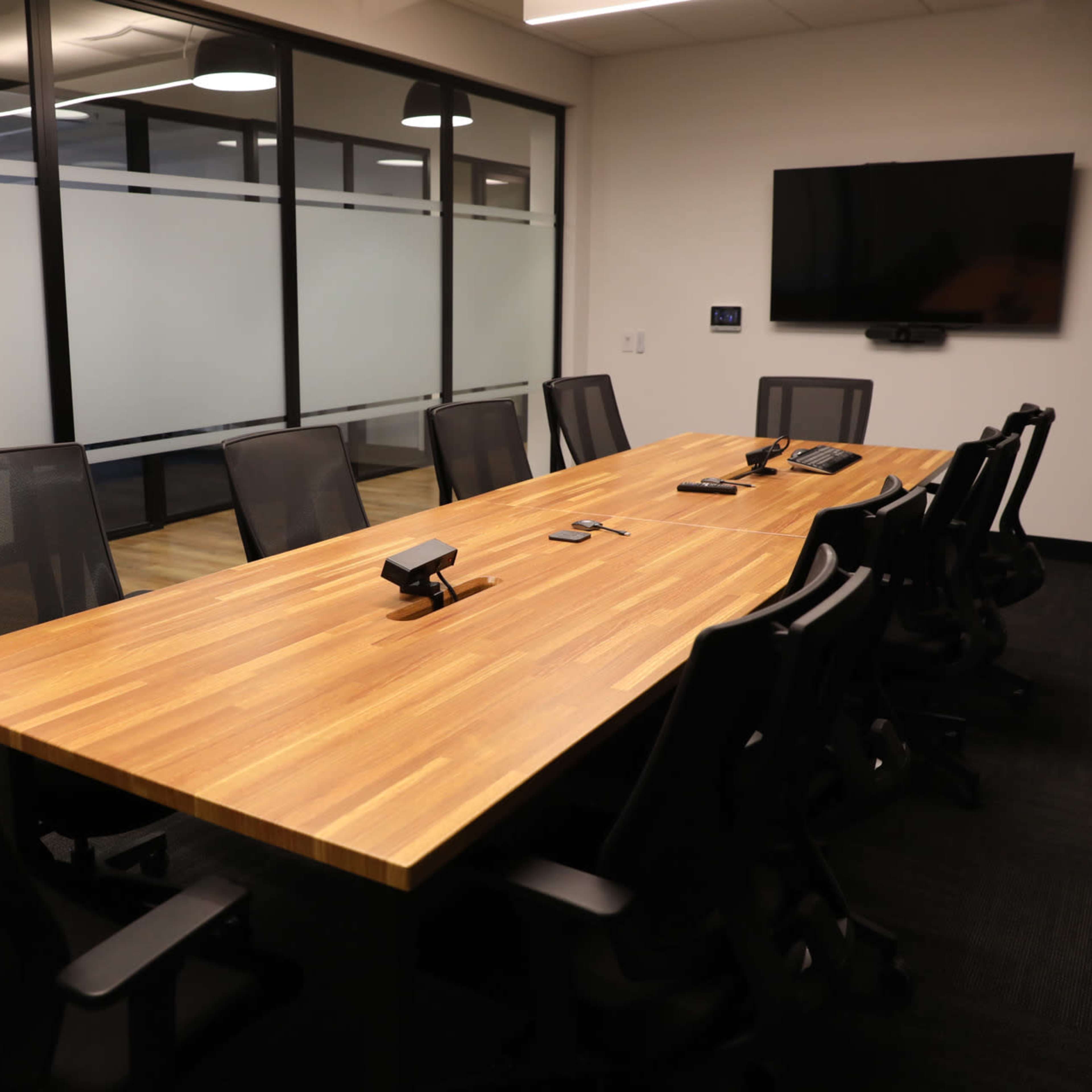 A large conference room features a wooden table surrounded by ergonomic chairs and a wall-mounted television.