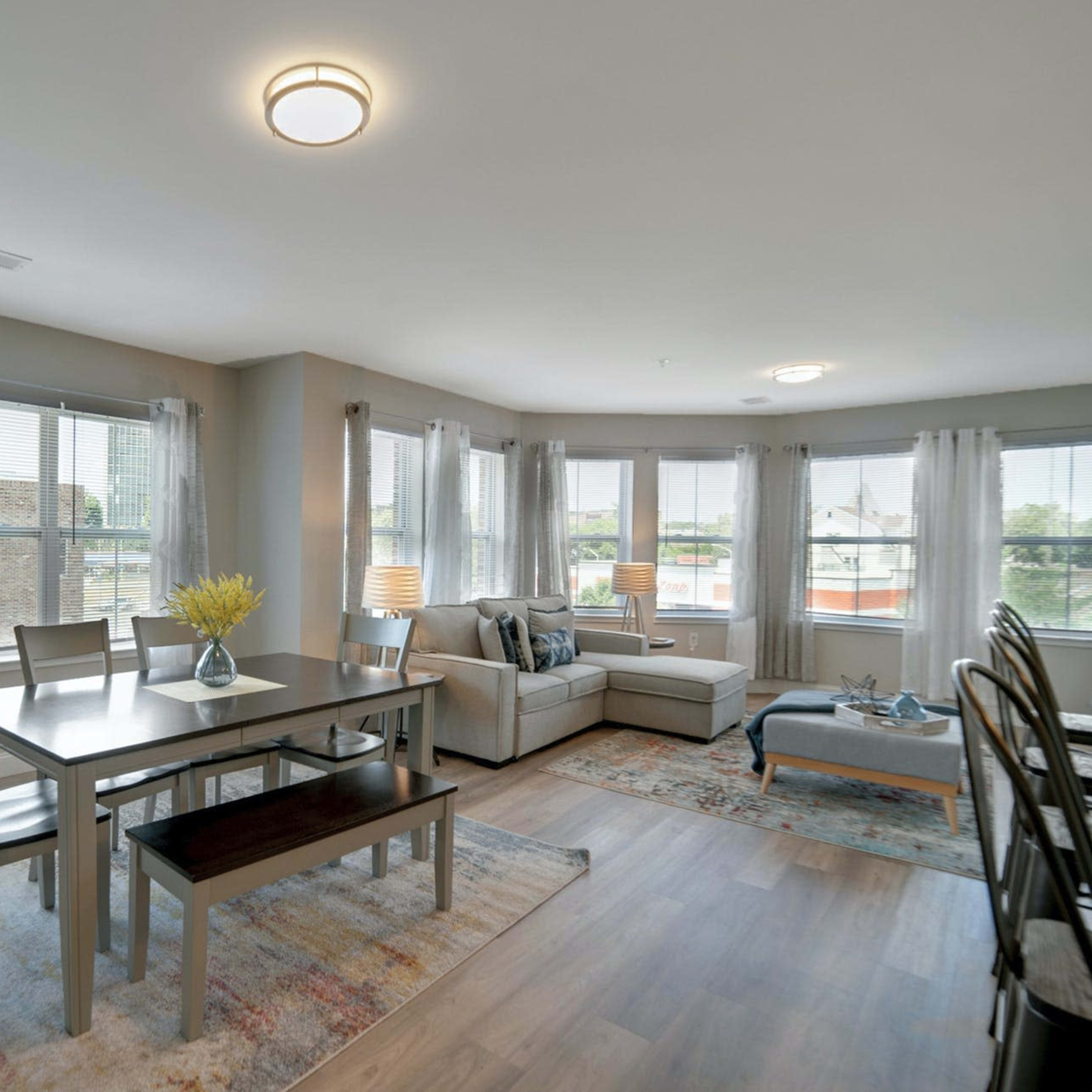 A modern living space features a dining area with a table and chairs, adjacent to a cozy seating arrangement with large windows allowing natural light.