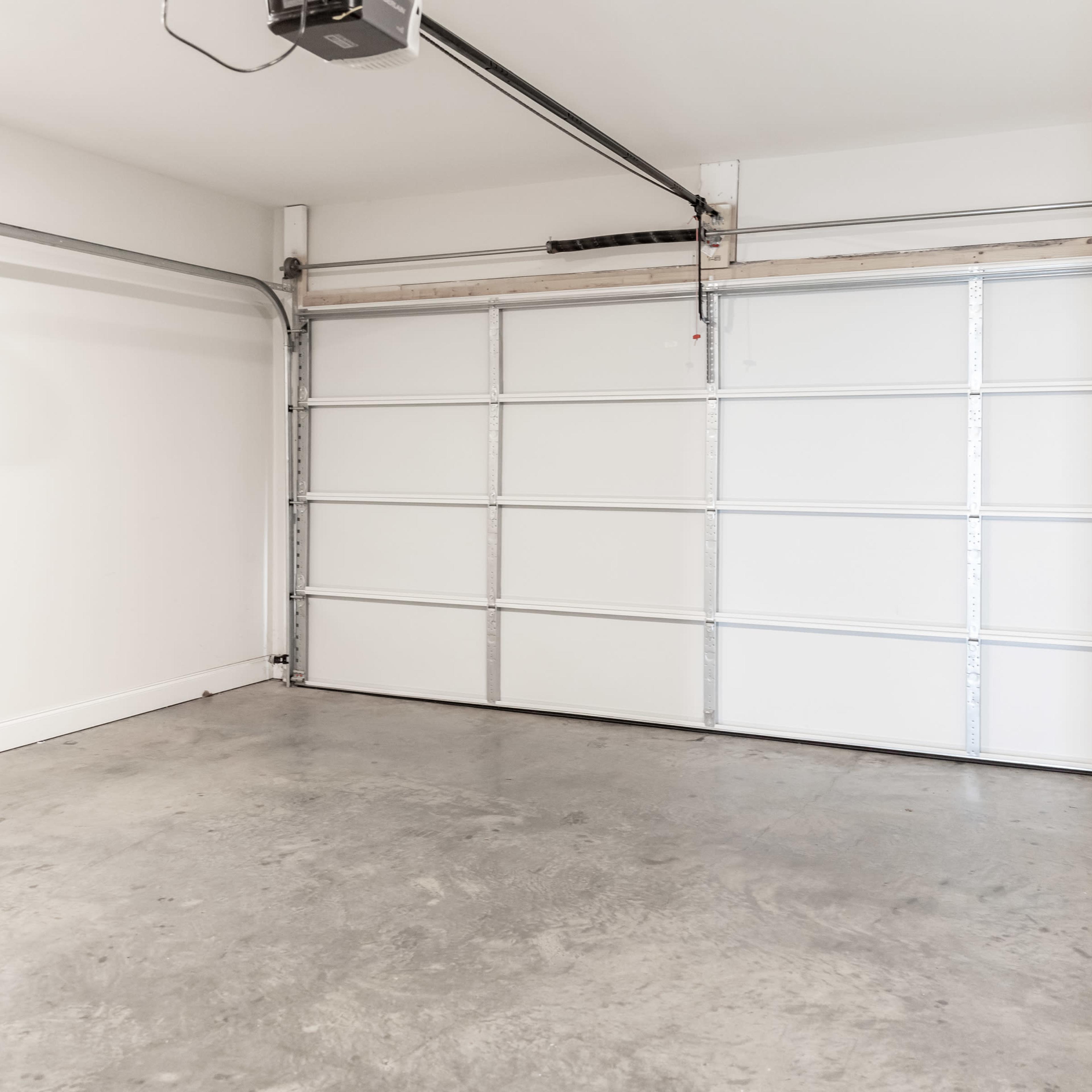An empty garage with a white garage door and concrete flooring.