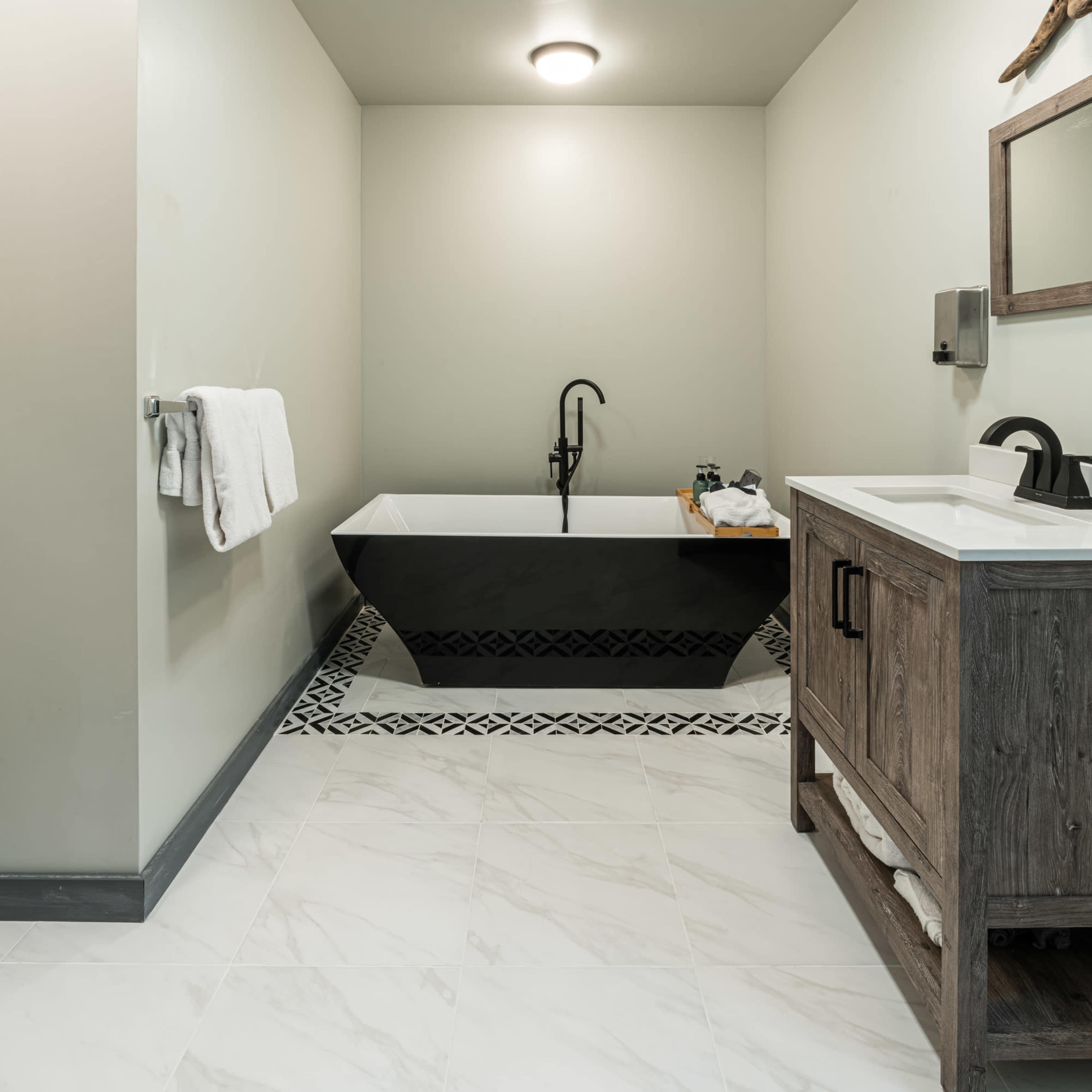 A minimalist bathroom featuring a black freestanding bathtub, a wooden vanity, and light-colored walls with tiled flooring.
