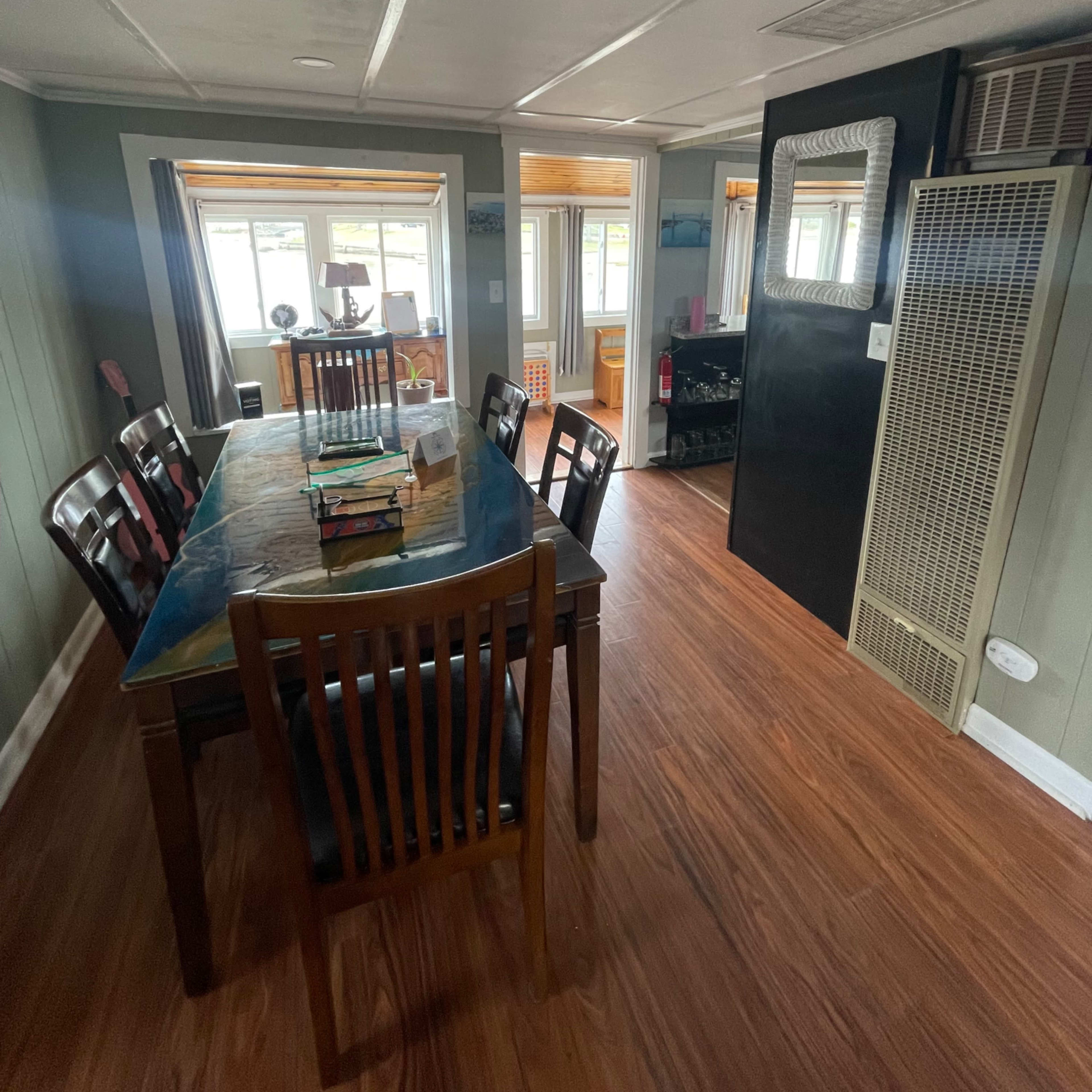 A dining area with a table and chairs, leading into a well-lit space featuring windows and a heater.