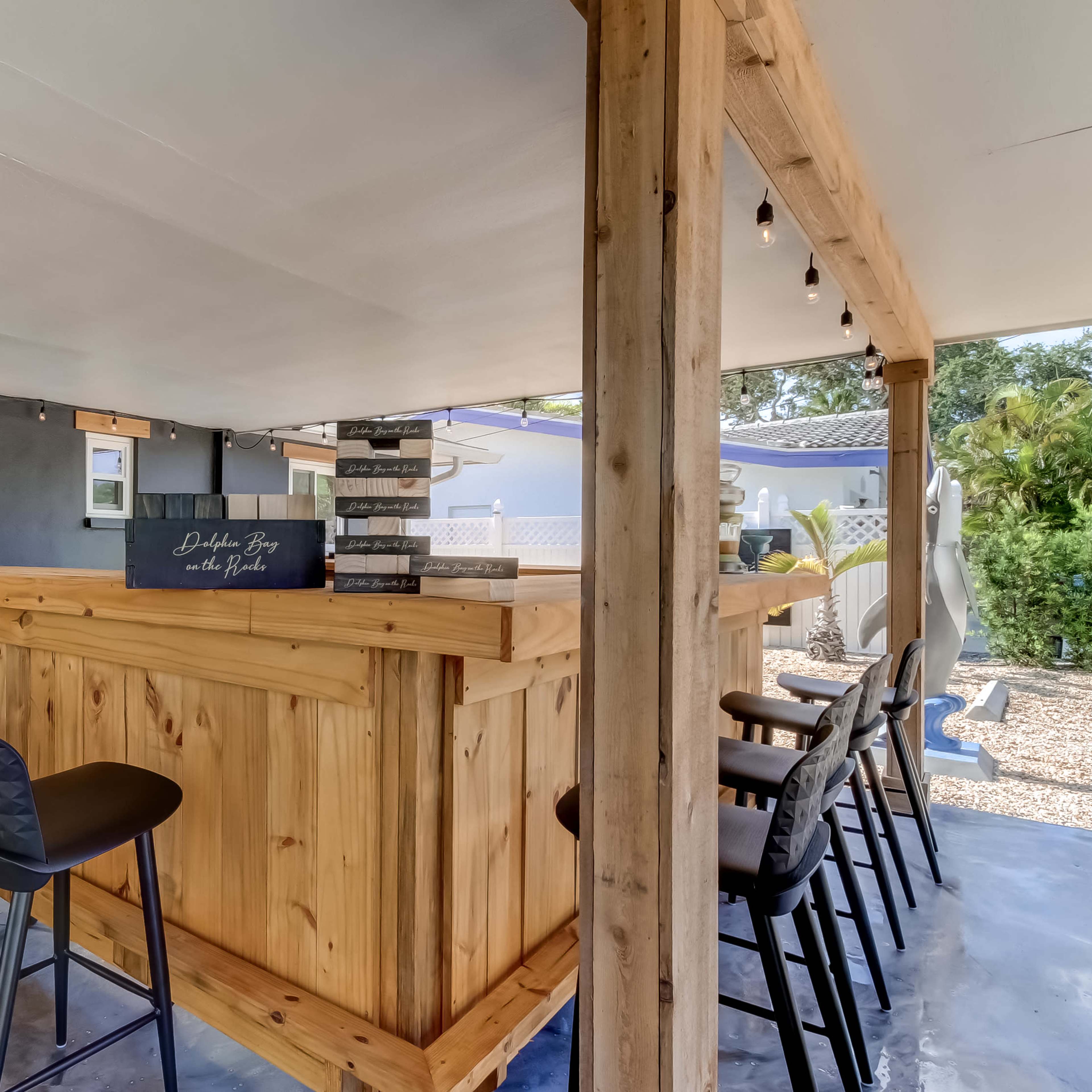 A wooden bar area with high chairs, surrounded by concrete flooring and an open space with outdoor access.