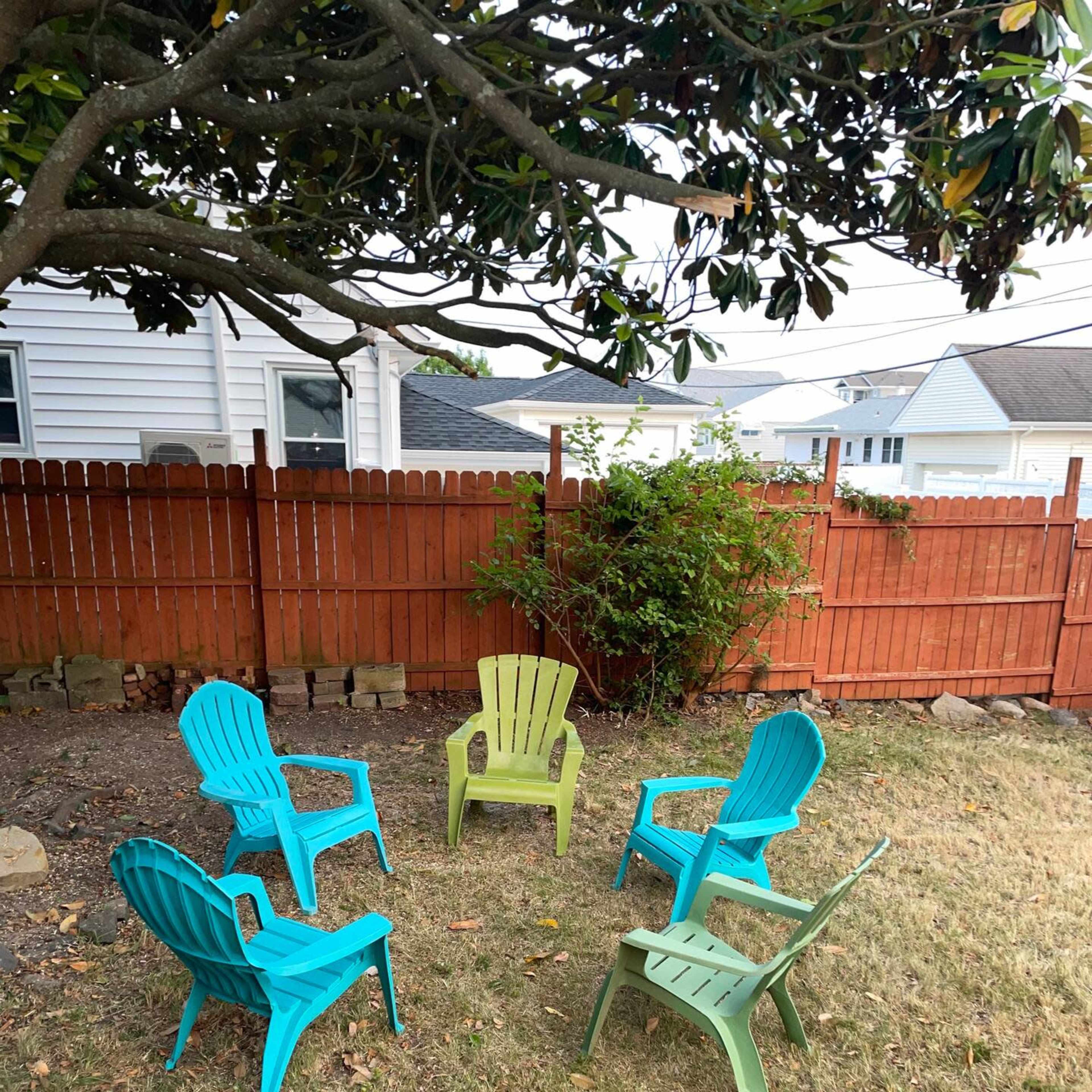 A circular arrangement of colorful plastic chairs is set on a grassy area within a fenced backyard.