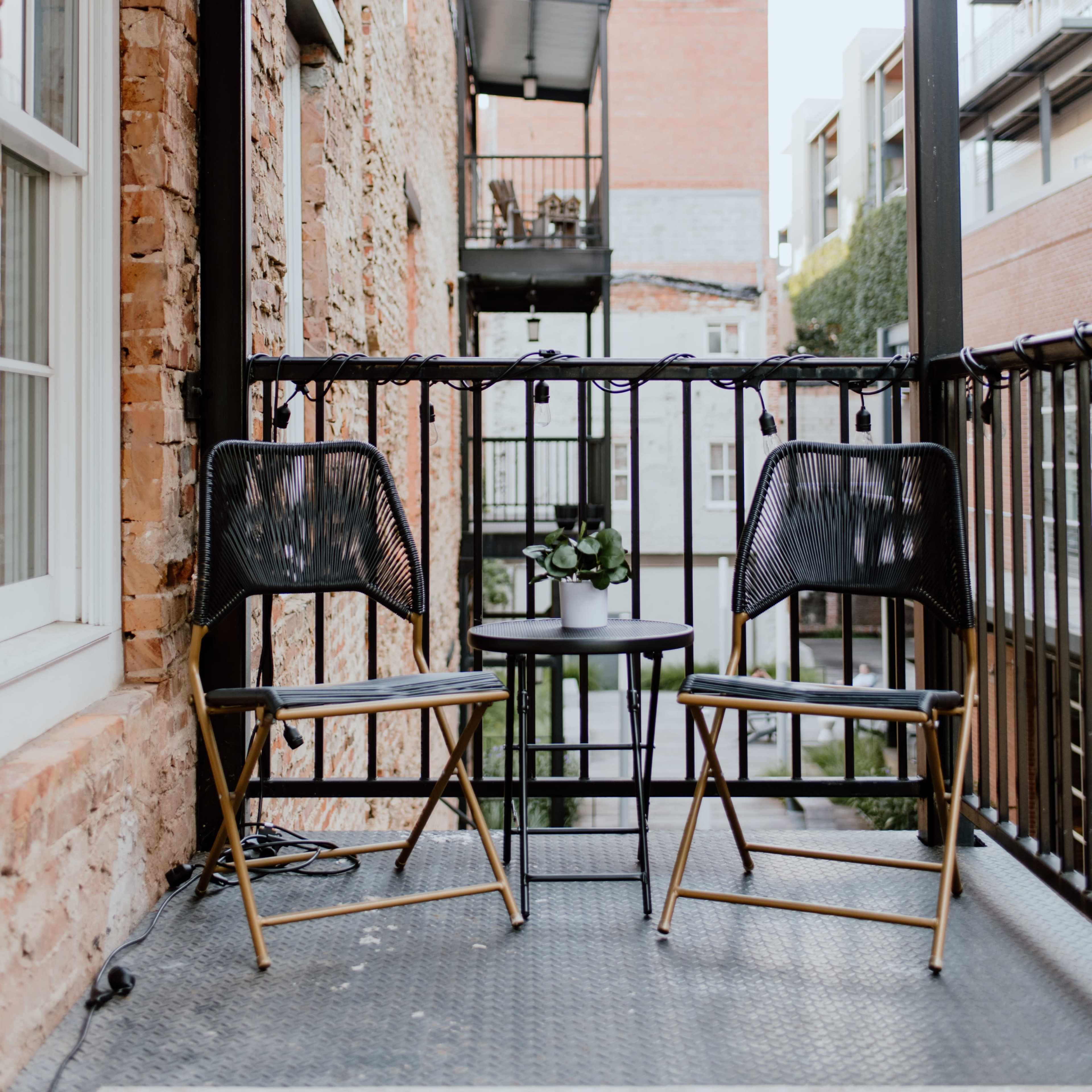 A small balcony with two black chairs and a round table, surrounded by brick buildings.