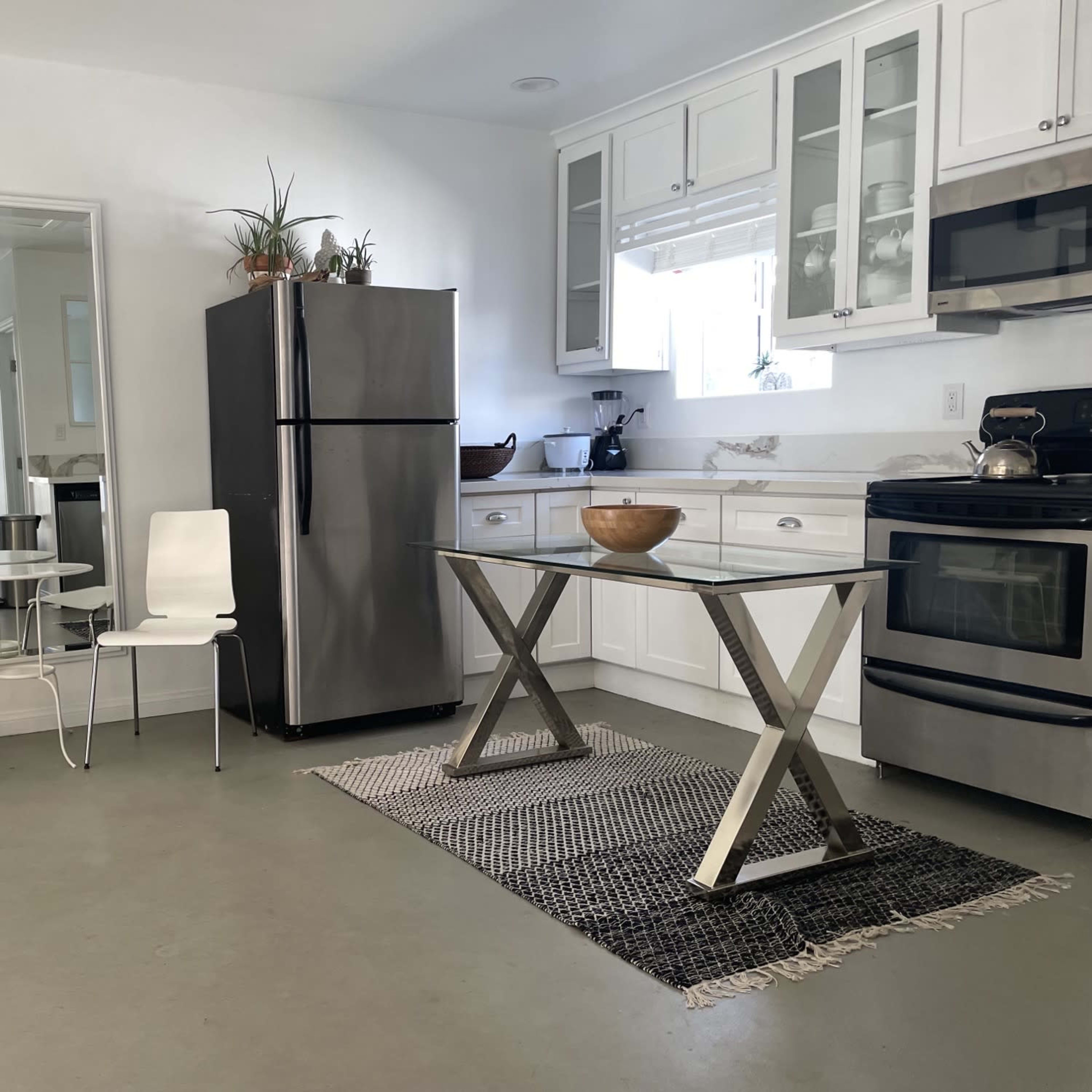 A modern kitchen with white cabinets, stainless steel appliances, a glass-top table, and two white chairs.