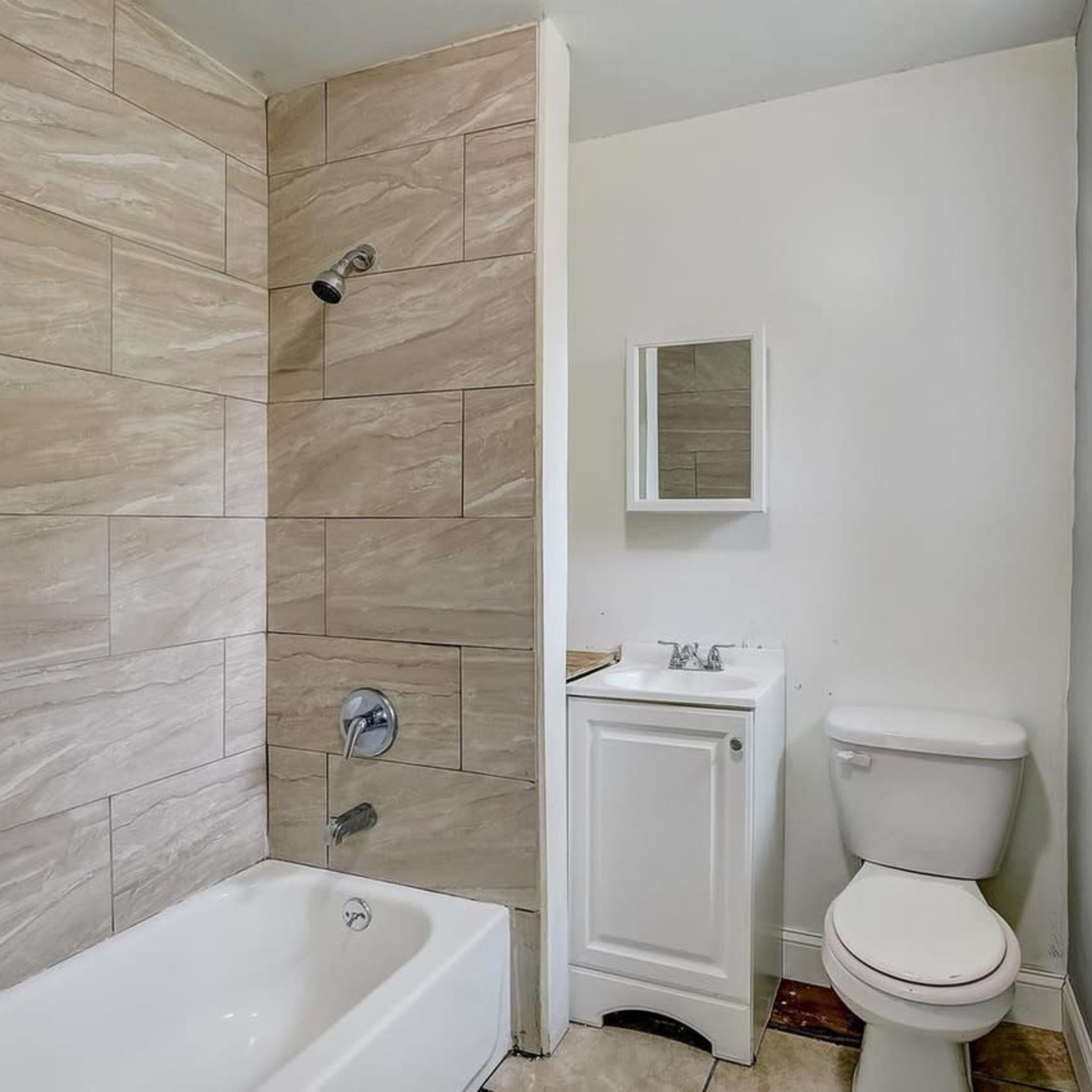 A bathroom featuring a bathtub with a shower, a toilet, and a small sink with a mirror.