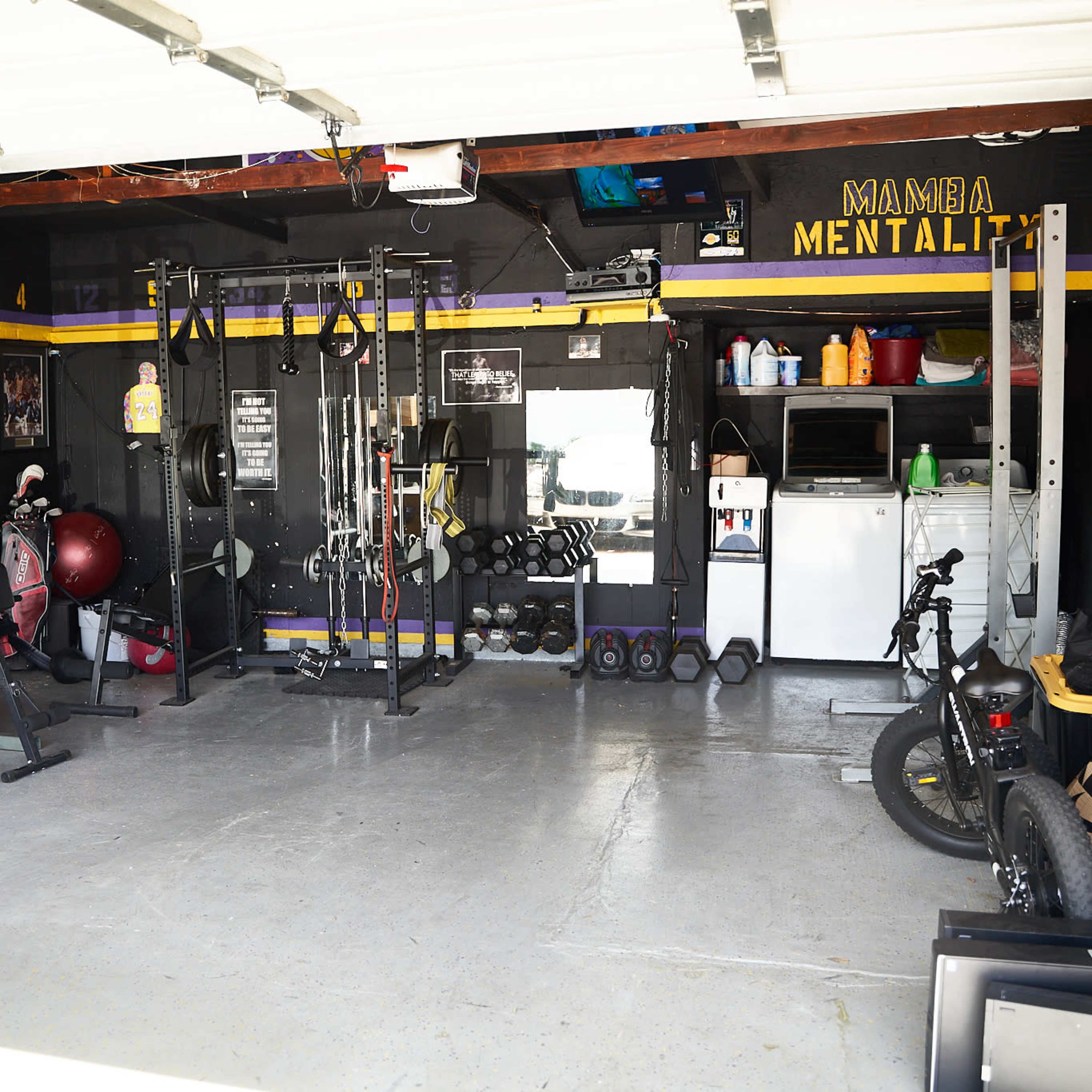A home garage gym space equipped with various fitness equipment, including weights, benches, and a stationary bike.