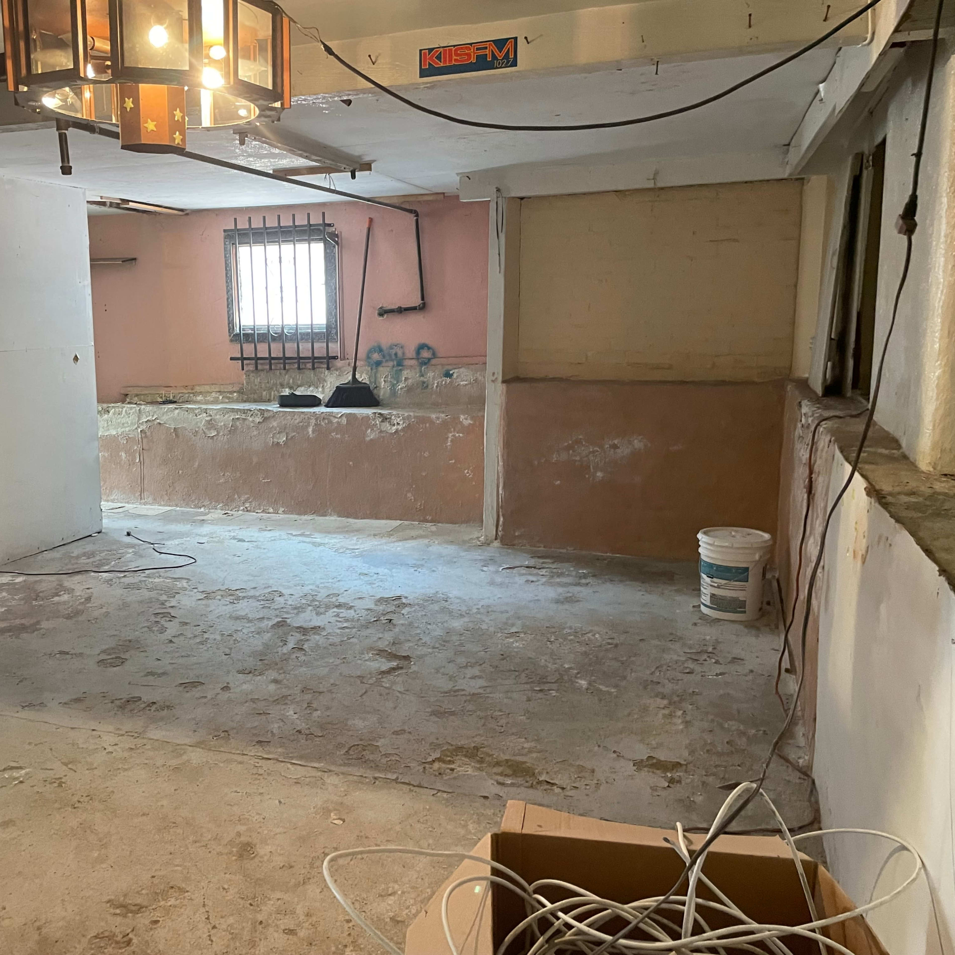 An empty basement with bare walls, scattered construction materials, and a small window at one end.