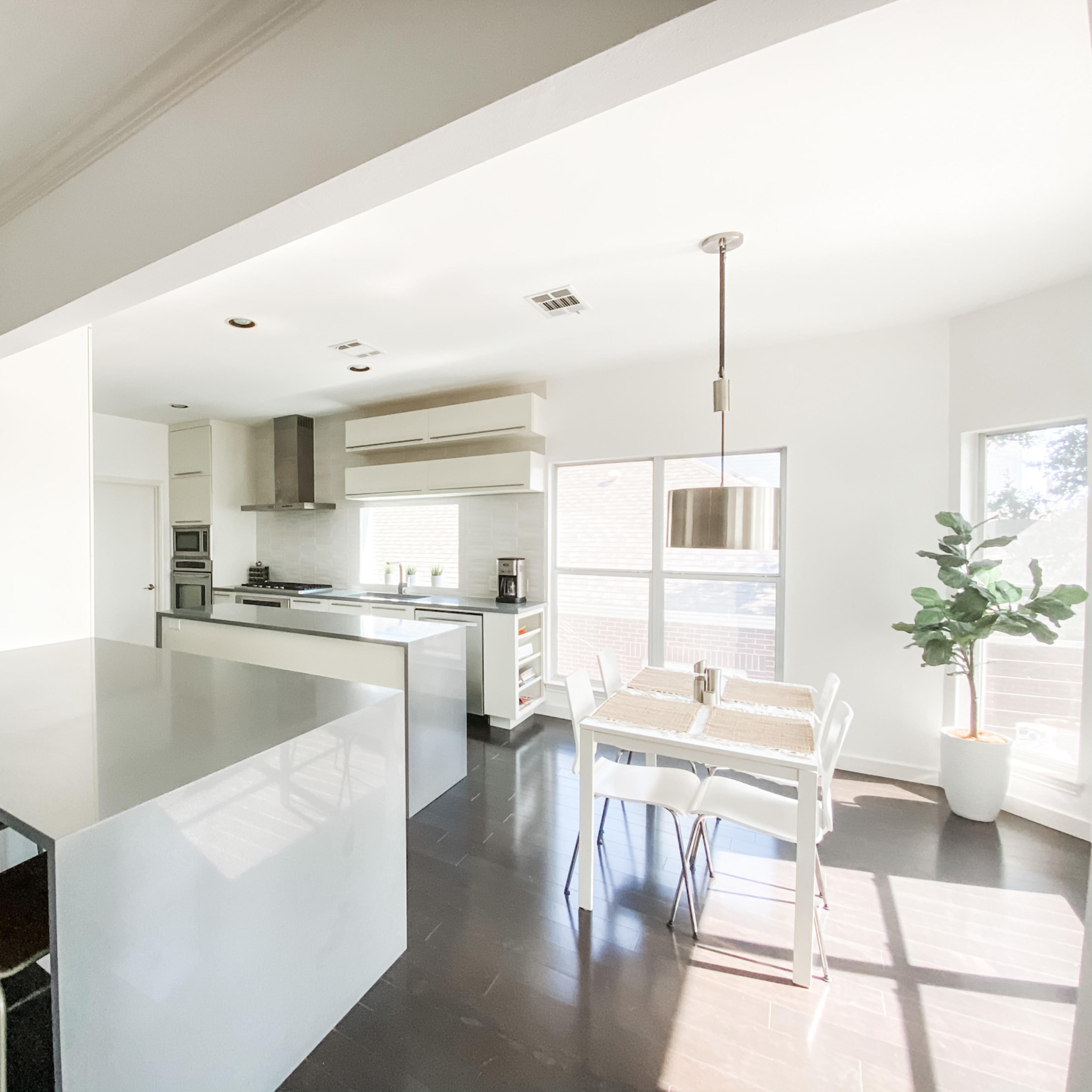 A modern kitchen features a large island, sleek cabinetry, and a dining area with a table and chairs beside a window.
