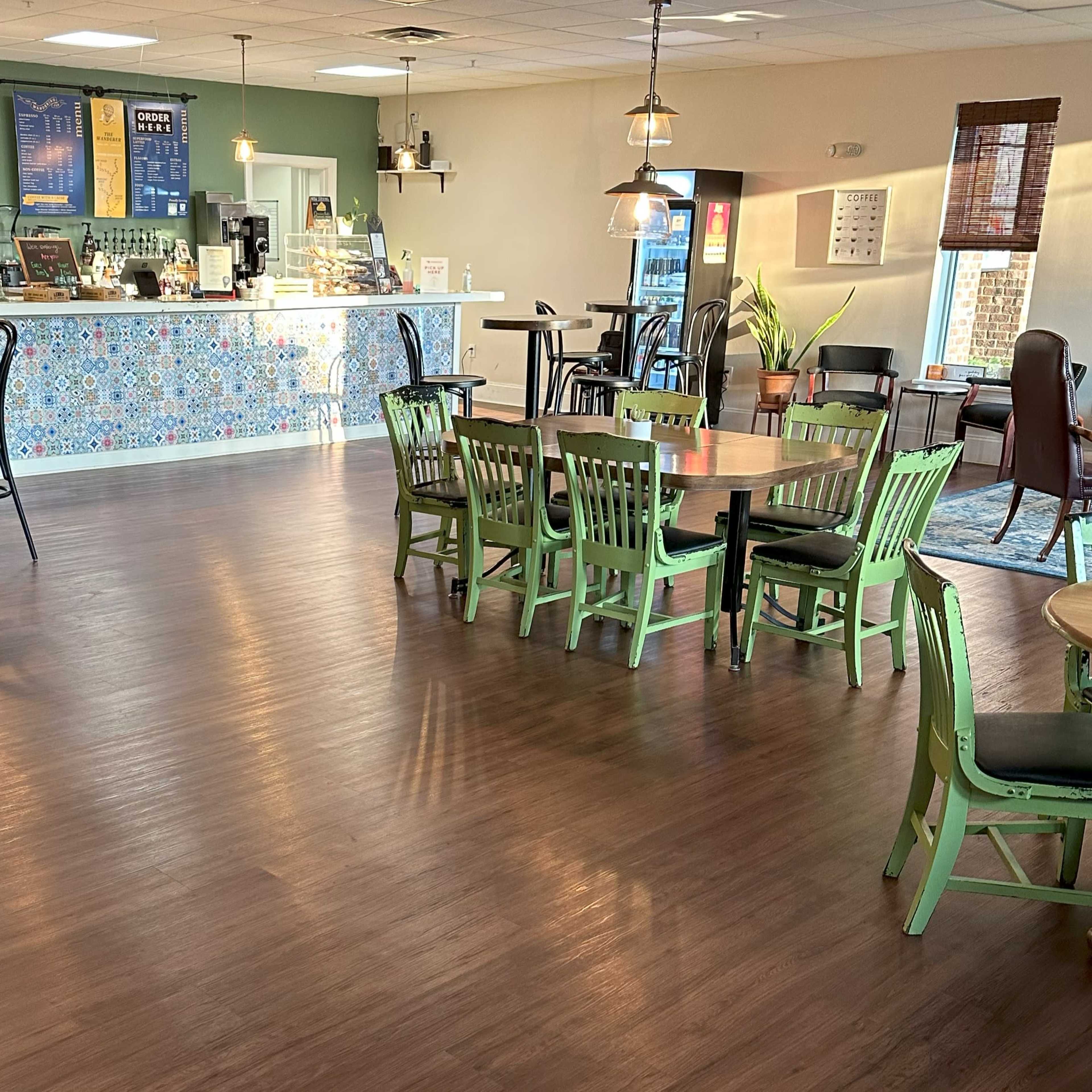 A cozy café interior with a counter displaying a menu and seating areas featuring green chairs and wooden tables.
