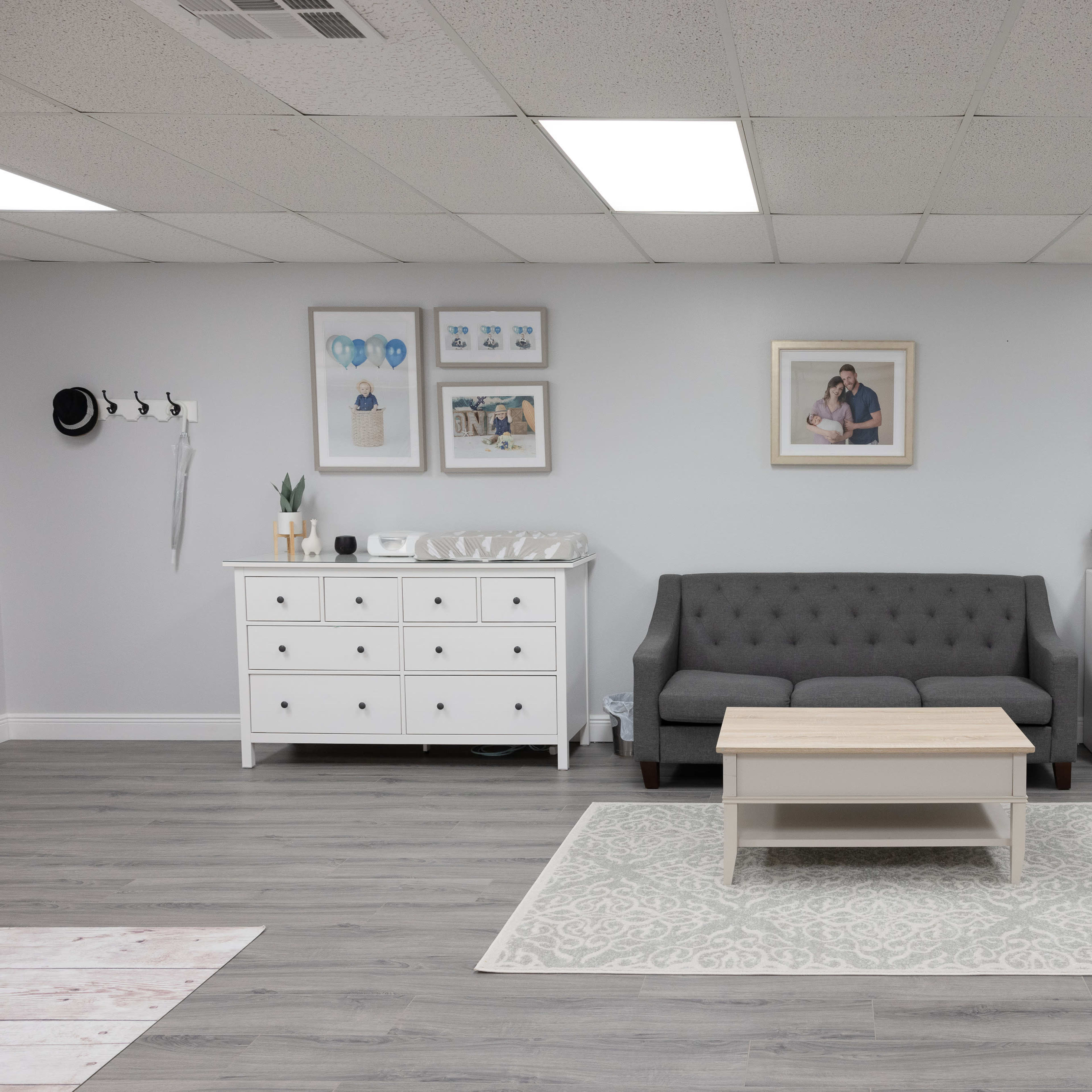 A modern, well-lit room with a gray sofa, a coffee table, and white furniture, including a dresser and a small refrigerator against the wall.