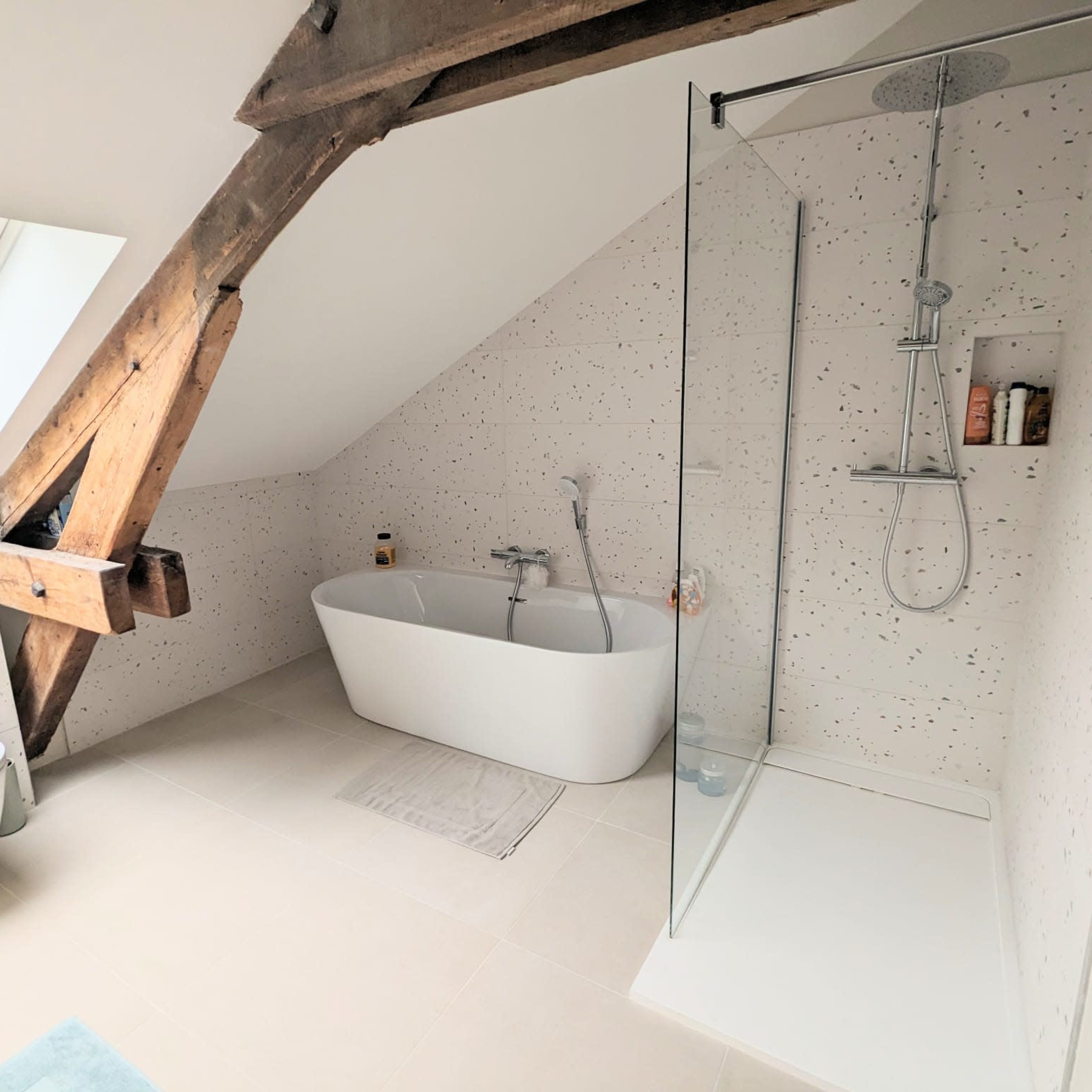 A modern bathroom featuring a freestanding bathtub, a glass shower enclosure, and exposed wooden beams.