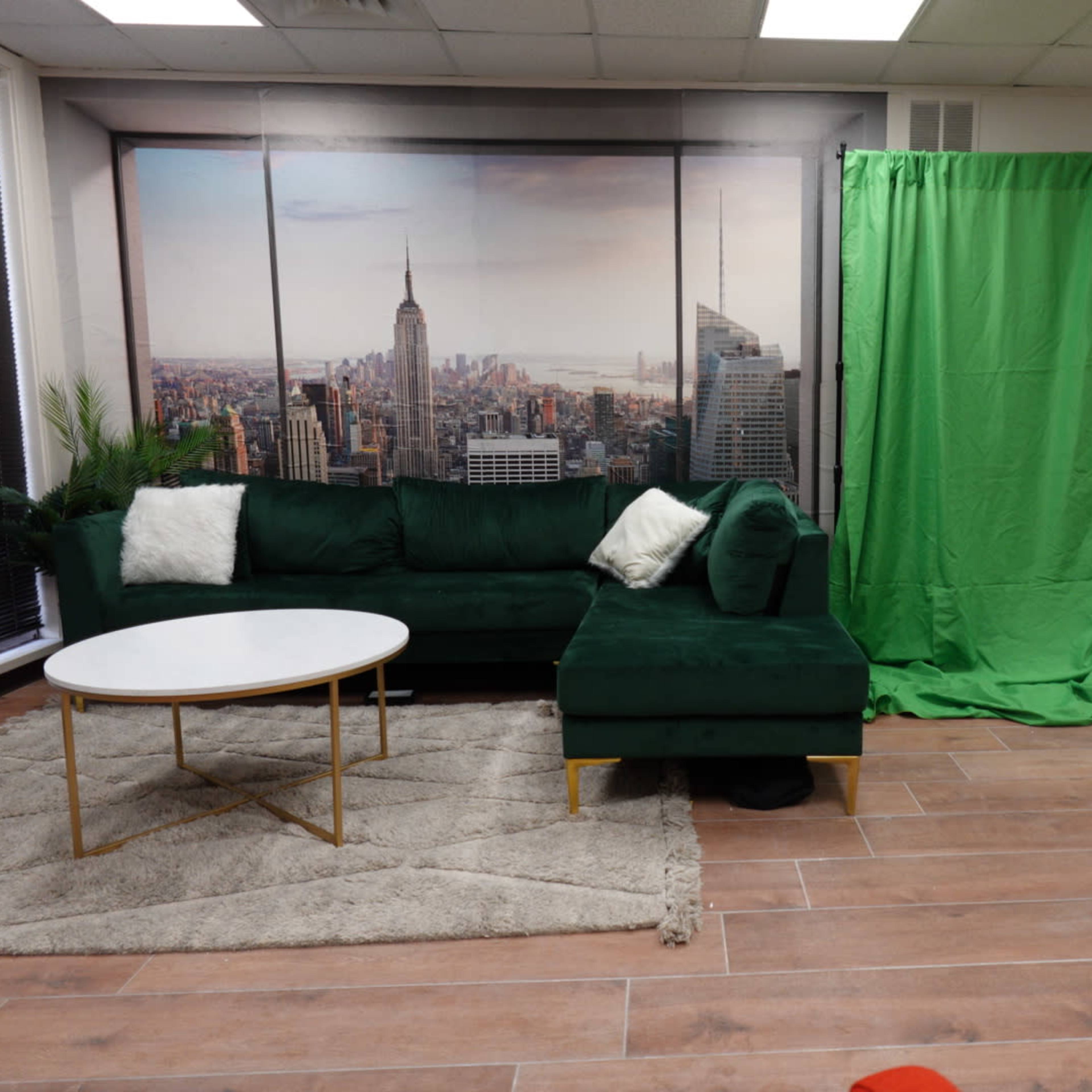 The scene features a green couch and a round white table on a rug, with a green backdrop to the right and a large cityscape mural on the wall behind.
