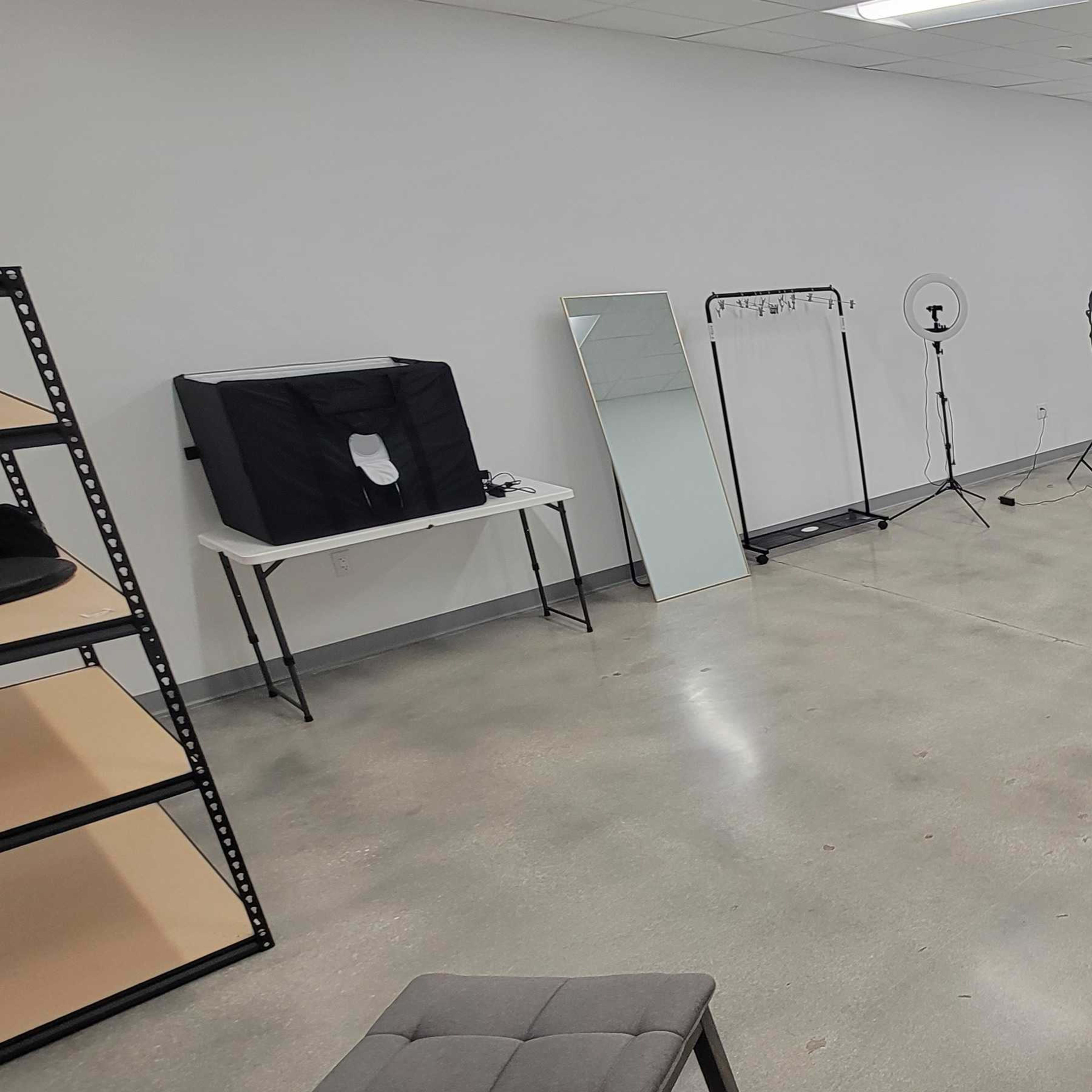 A blank studio space with a concrete floor, various lighting equipment, a mirror, and a backdrop setup against the walls.
