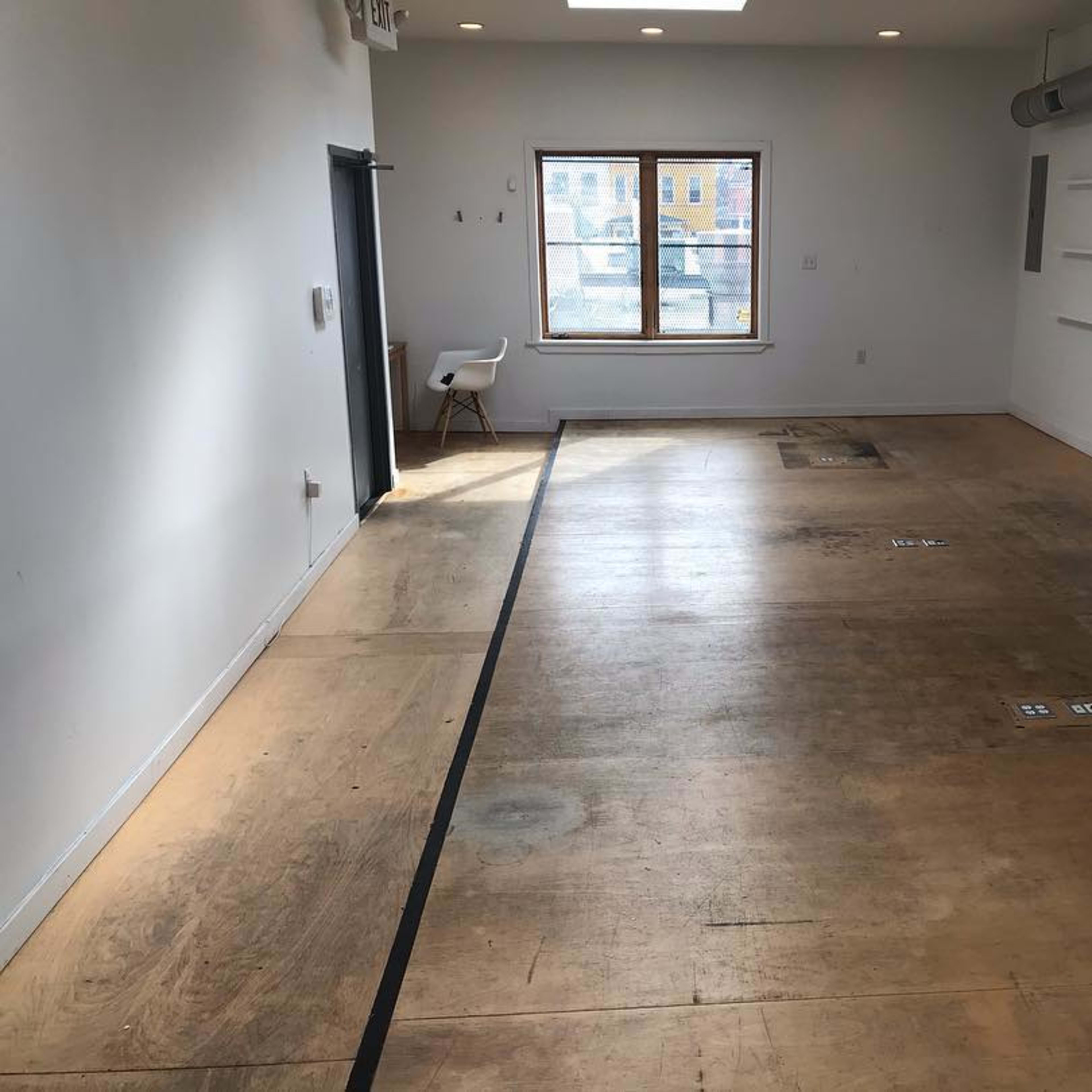 An empty room with a large window, wooden flooring, and minimal furnishings.