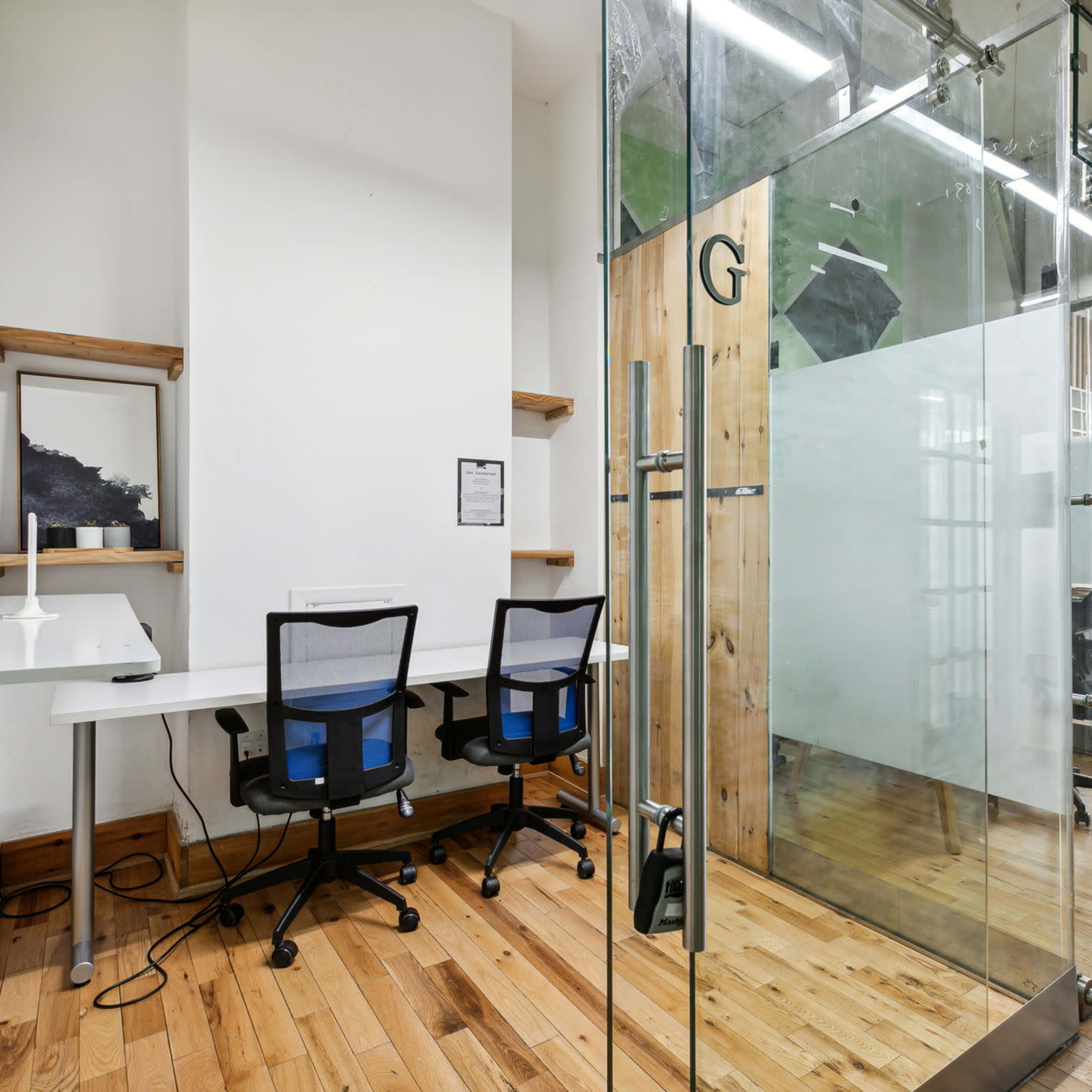 A modern office space featuring a glass meeting room and two black office chairs at a white desk.