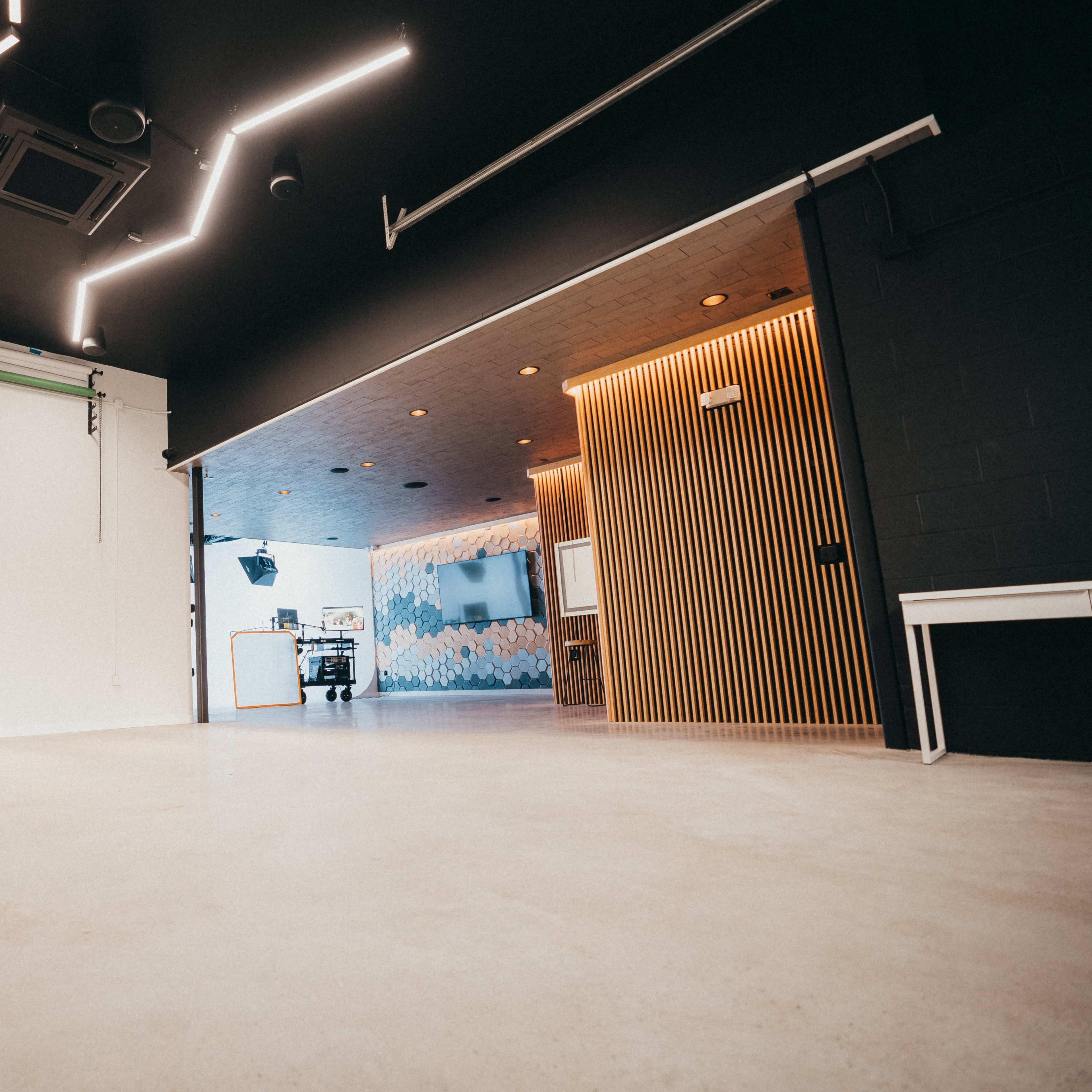 A spacious, evenly lit studio featuring a lighting setup on a stand and a split design with one side having a black wall and the other side showing a patterned mural.