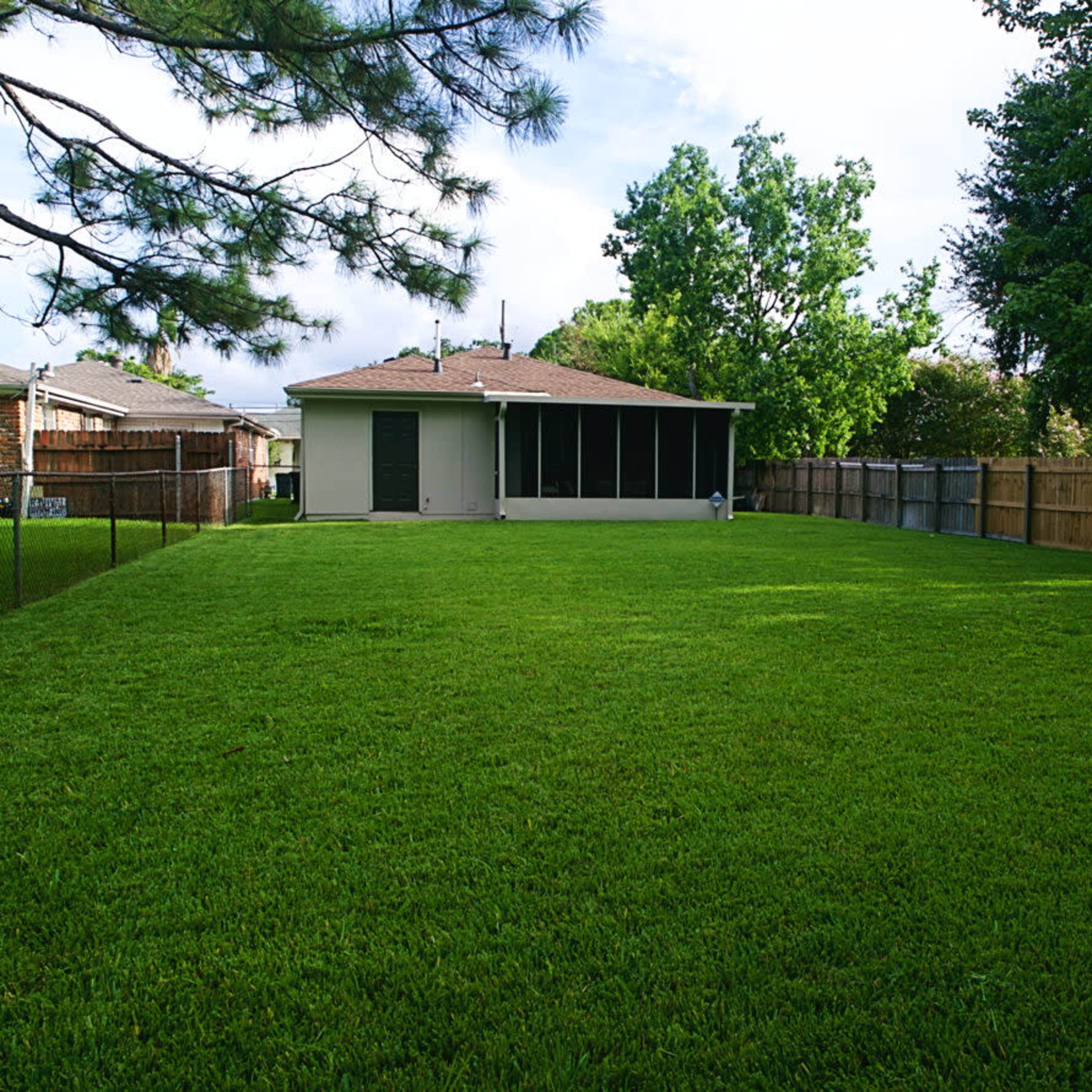 A spacious backyard with a well-maintained green lawn, fenced perimeter, and a single-story house in the background.