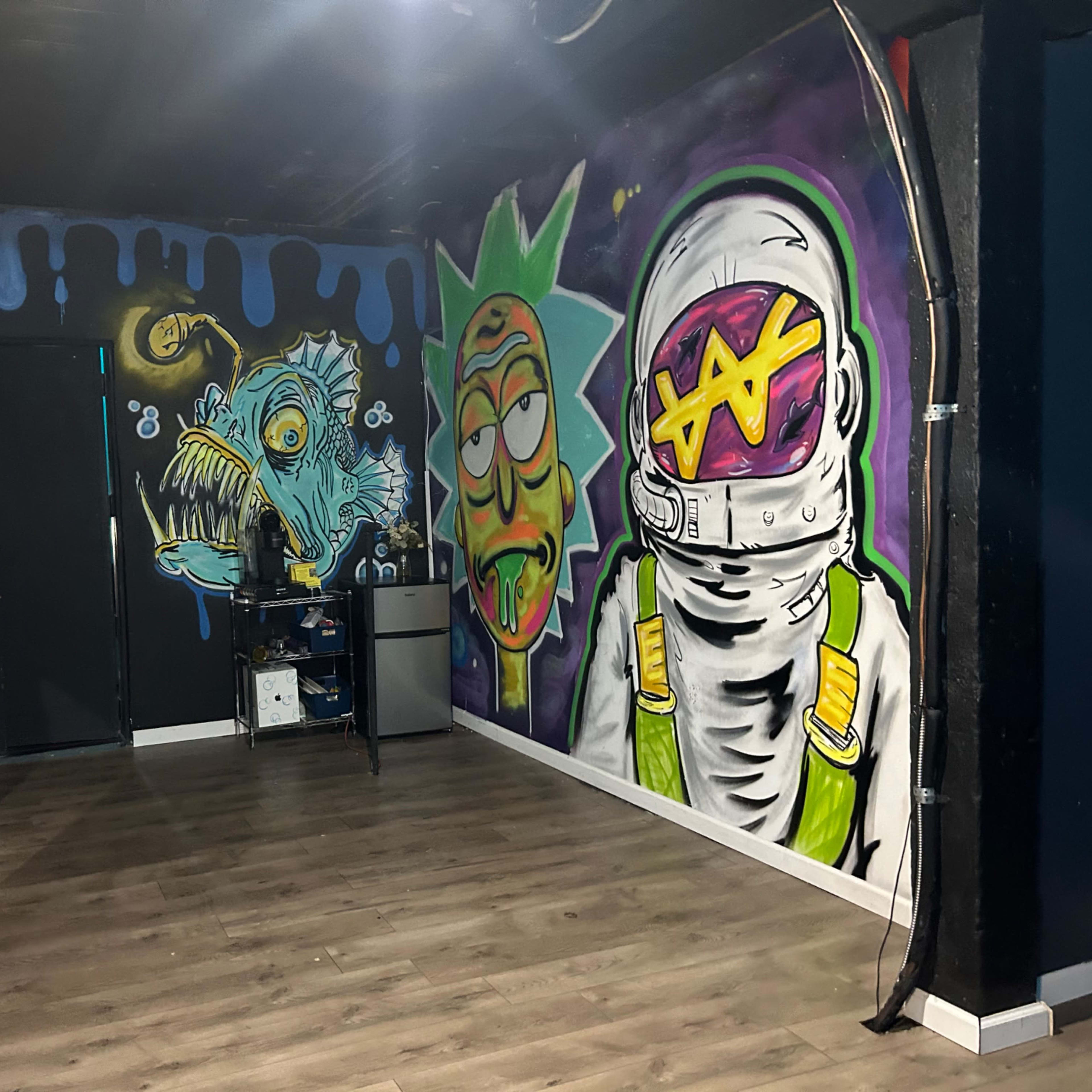 A room with vibrant graffiti murals on the walls, depicting a cartoonish astronaut and a character resembling a green-haired figure, along with a stylized monster, in front of a dark backdrop.