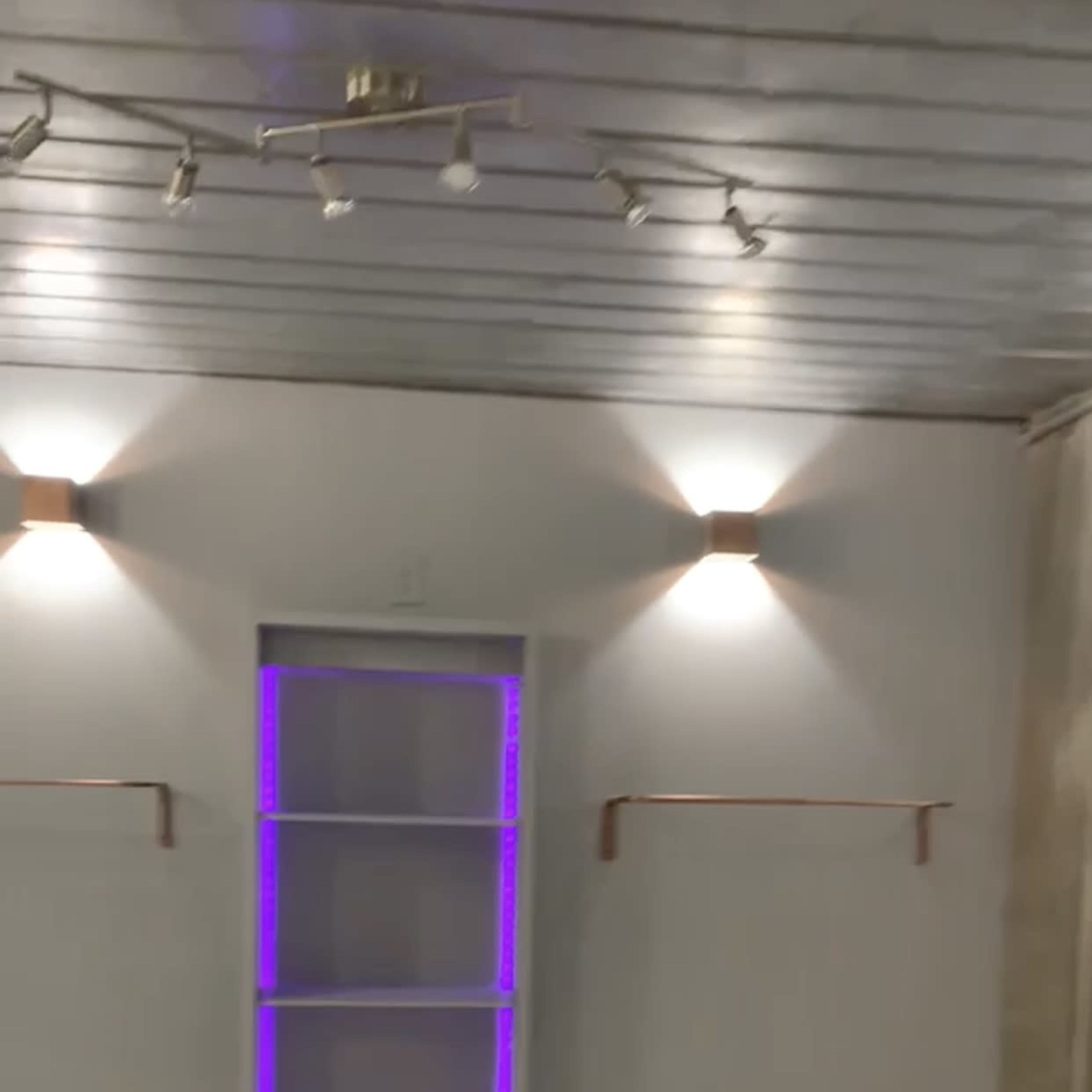 A blank room with gray walls, white flooring, and a window framed with purple lighting, flanked by two wall-mounted shelves.
