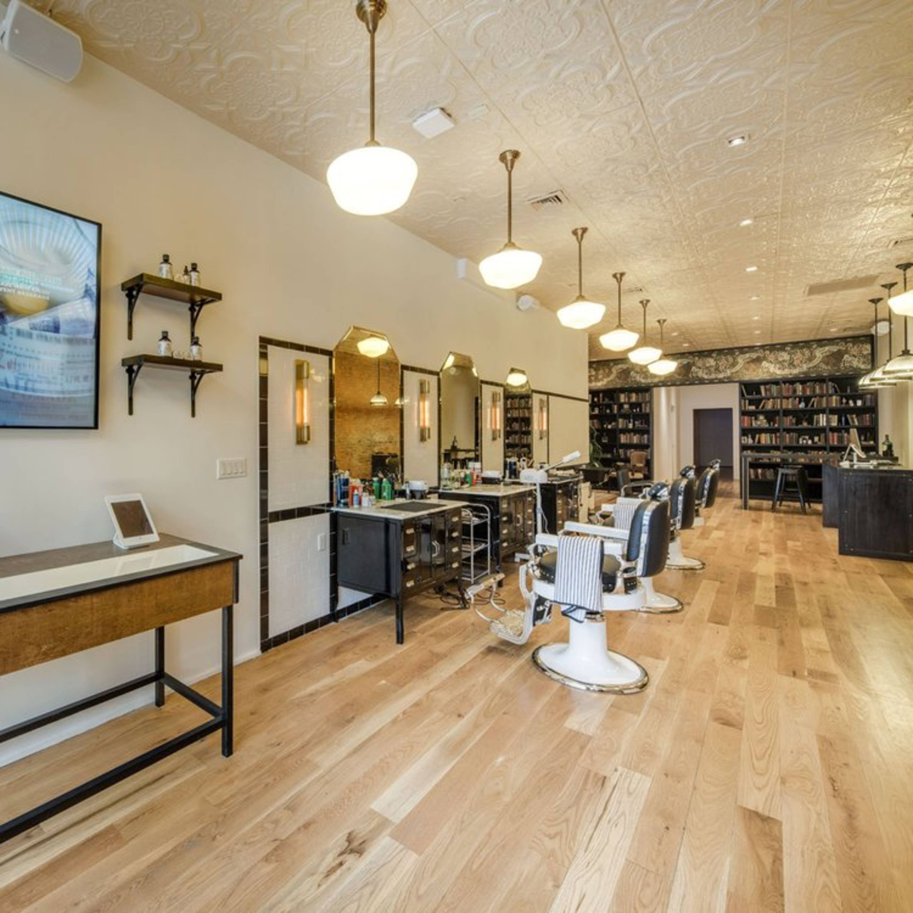 A modern hair salon with wooden flooring, styled chairs, wall-mounted shelves, and bright overhead lighting.