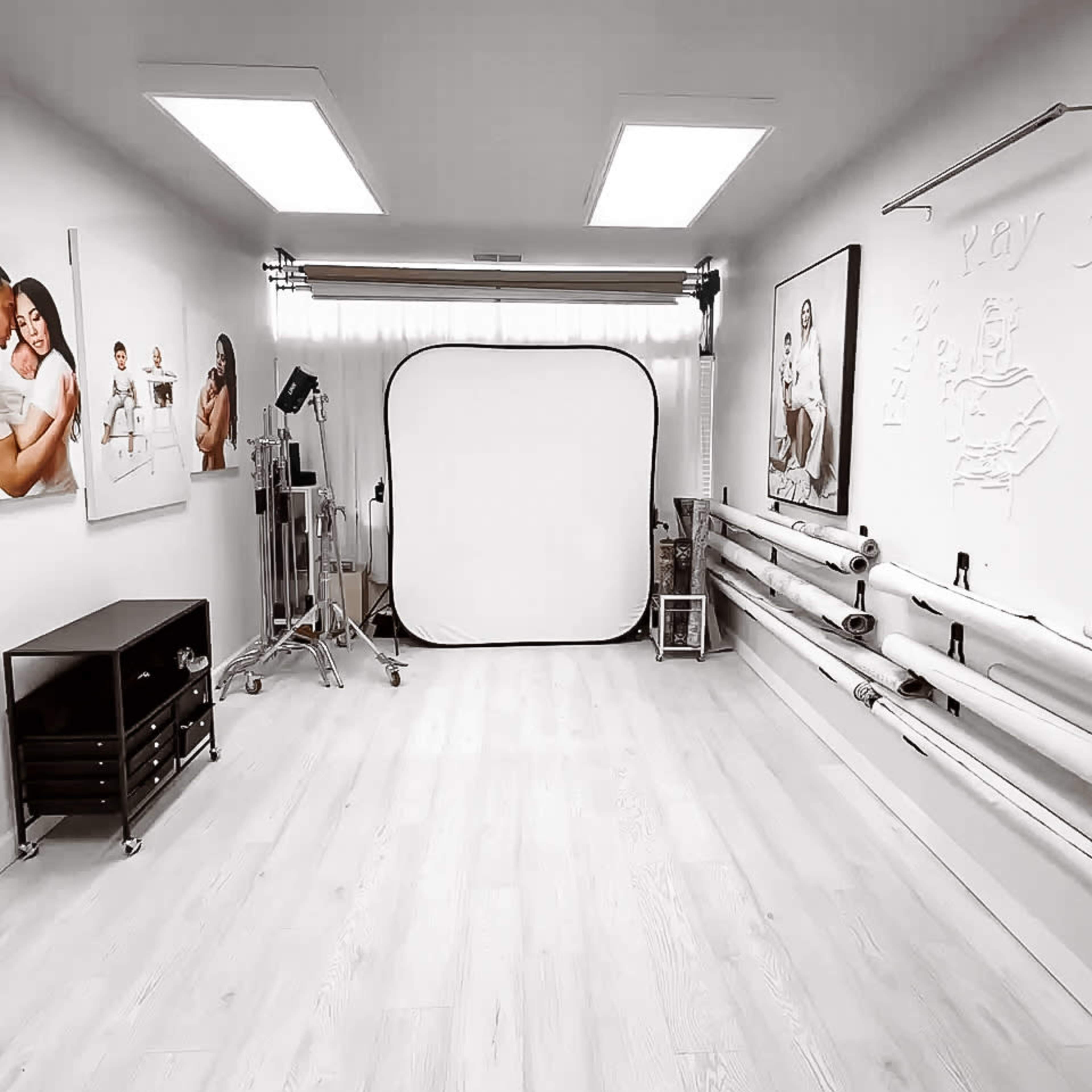 A photography studio with a large backdrop, lighting equipment, and various rolls of materials along the wall.