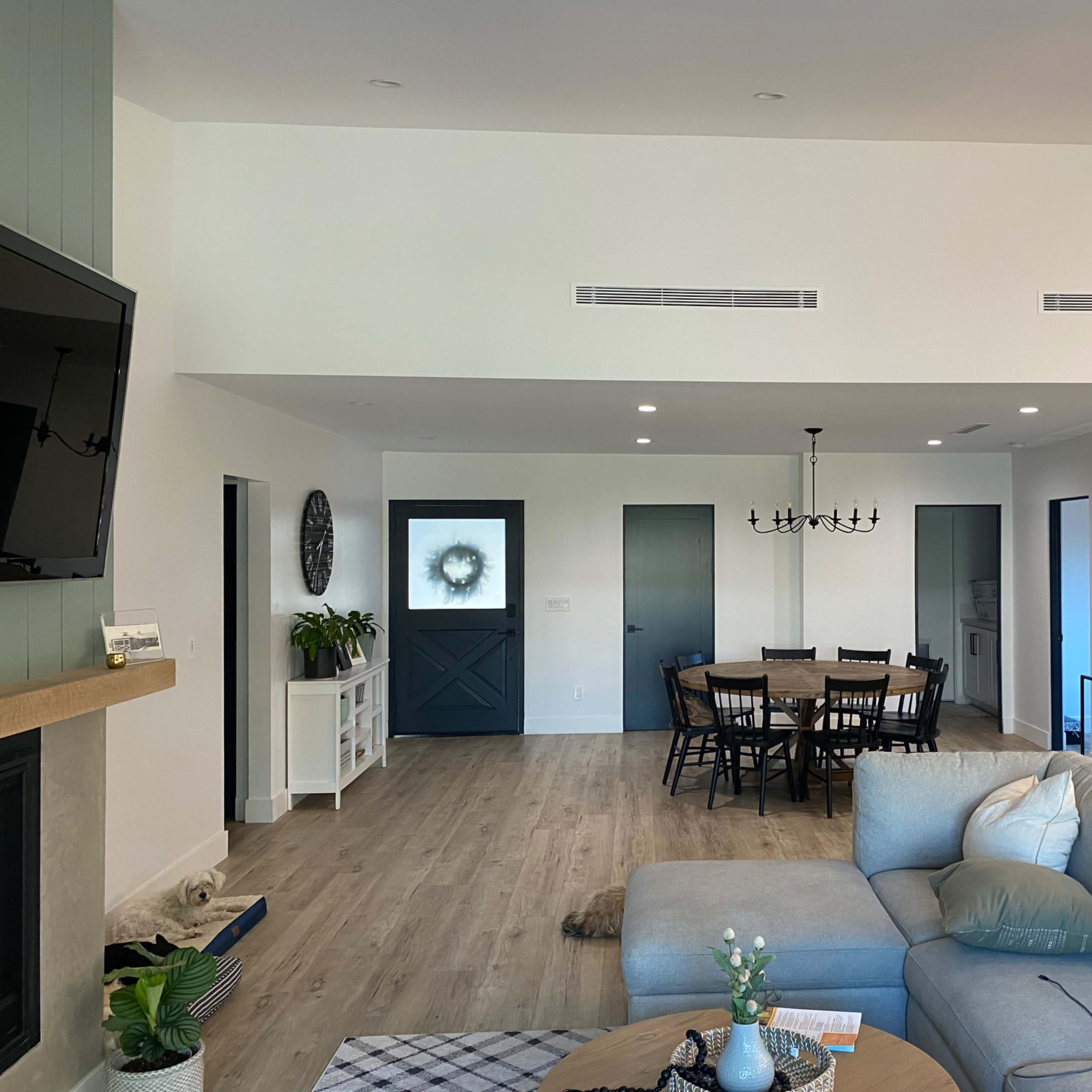 A modern open-concept living area featuring a sectional sofa, a dining table with chairs, and a doorway leading to a kitchen space.