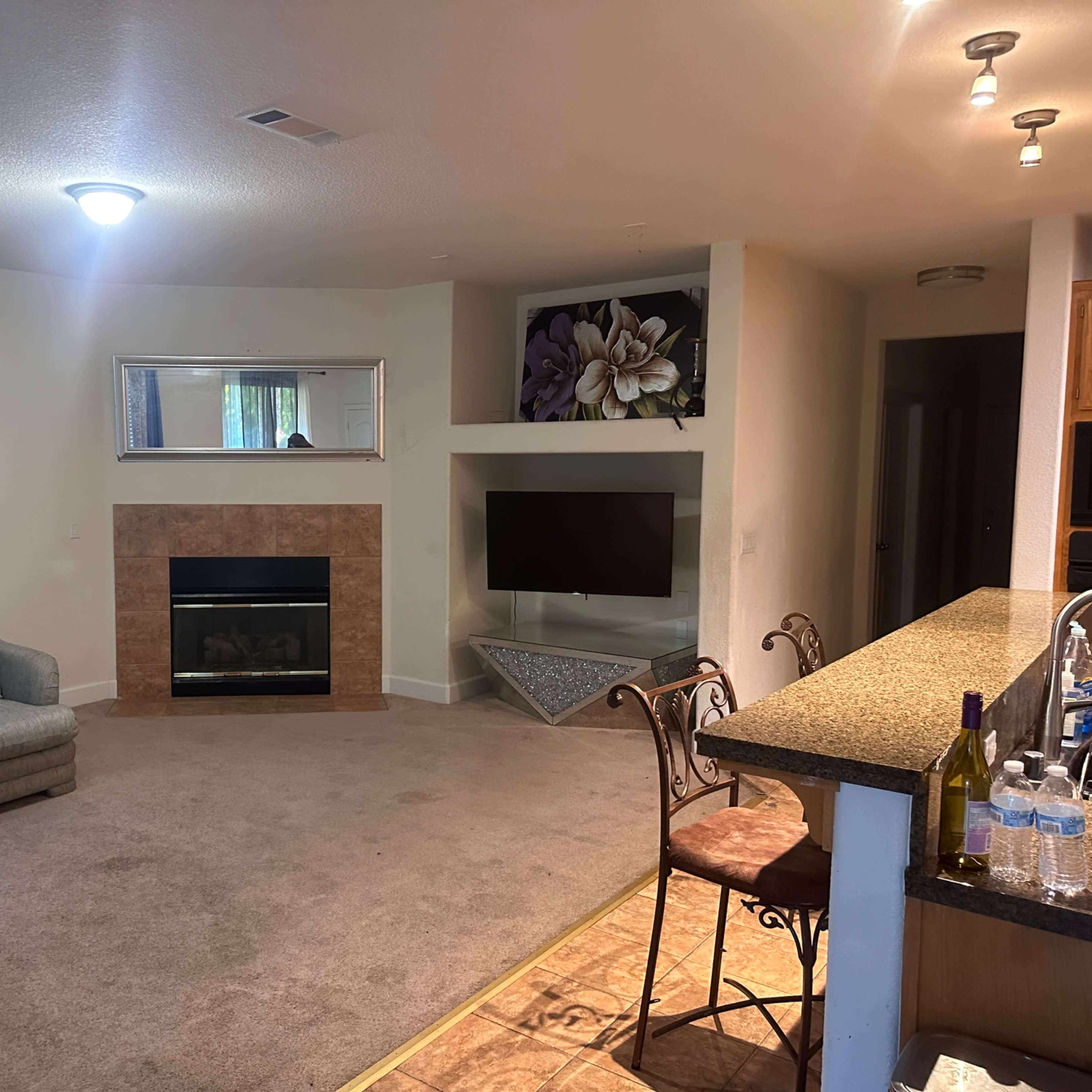 A living room with a sectional sofa, a fireplace, a mounted television, and a kitchen counter with bar stools.