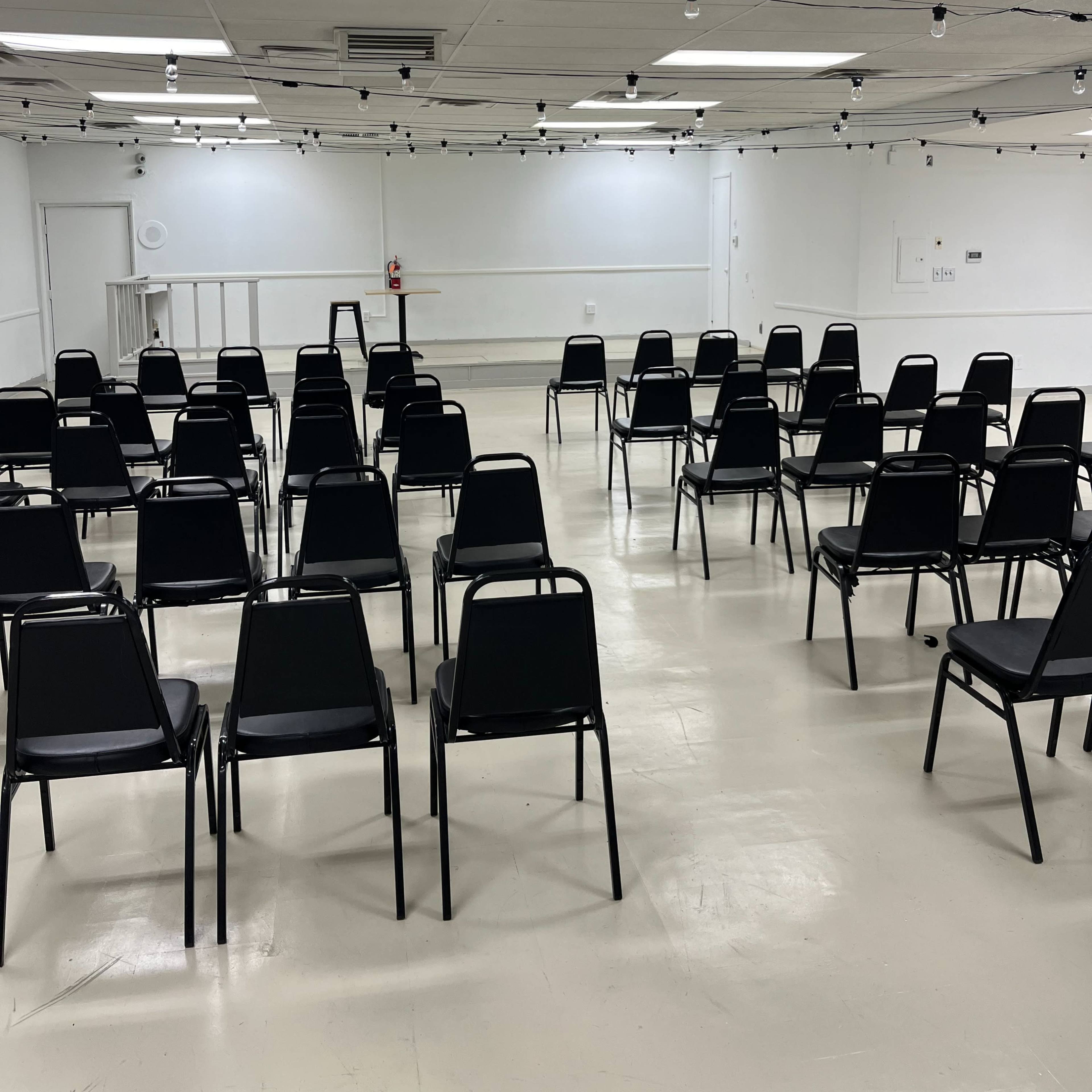 A spacious, white room arranged with neatly aligned black chairs facing a blank wall.