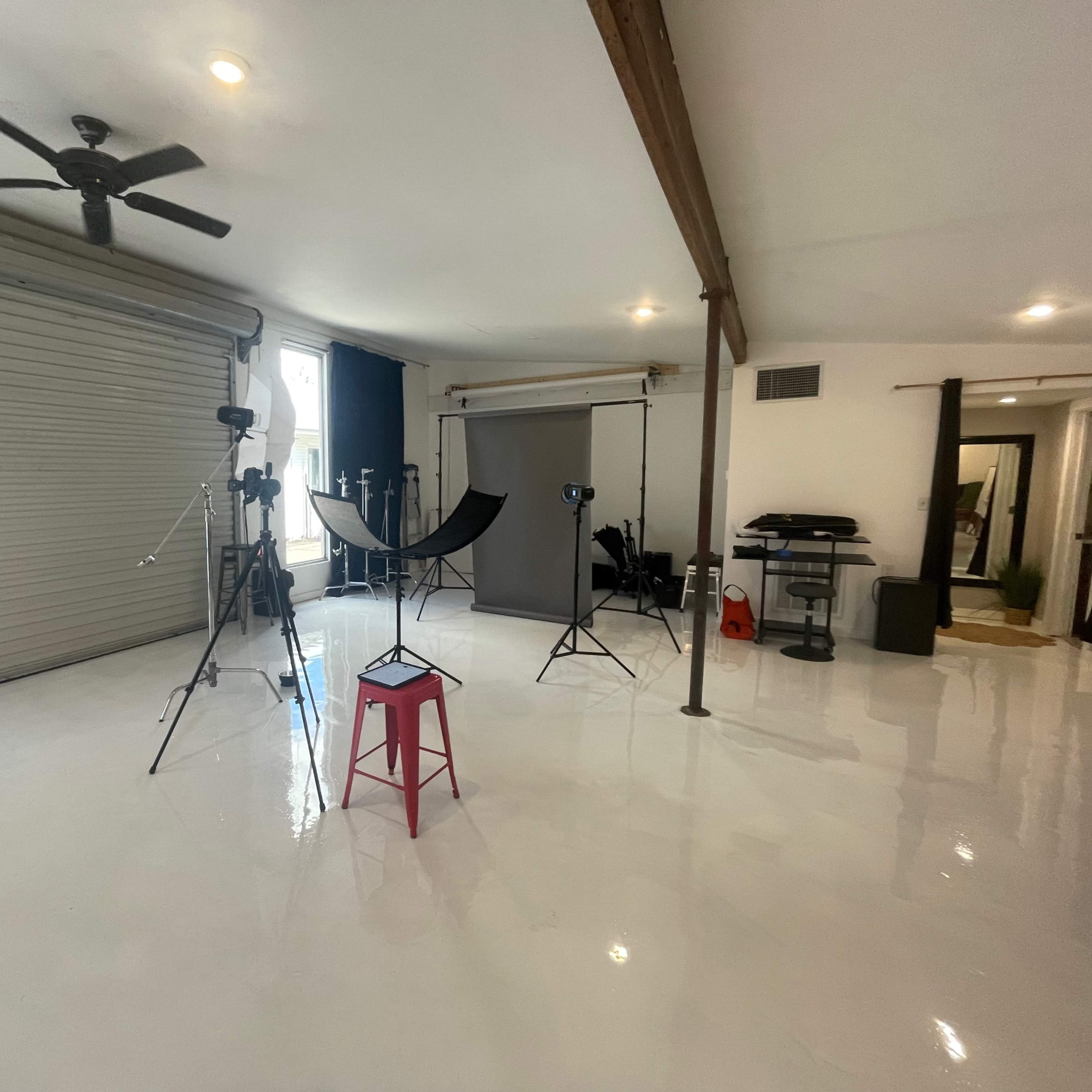 A well-lit studio space with photography equipment, including tripods, softboxes, and a backdrop setup, along with a pink stool in the center.