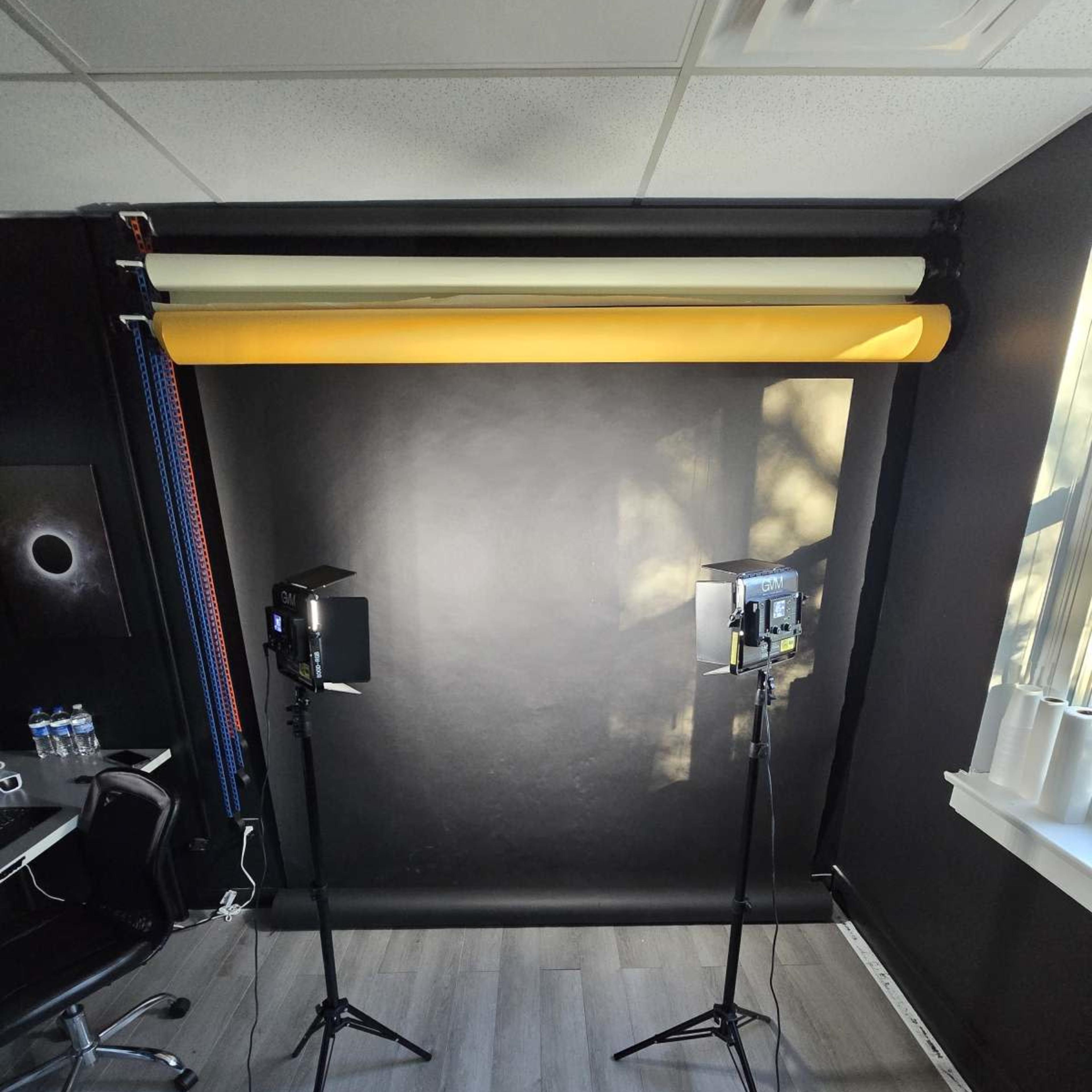 A photography studio setup with two lights on stands facing a black backdrop and a roll of yellow paper.