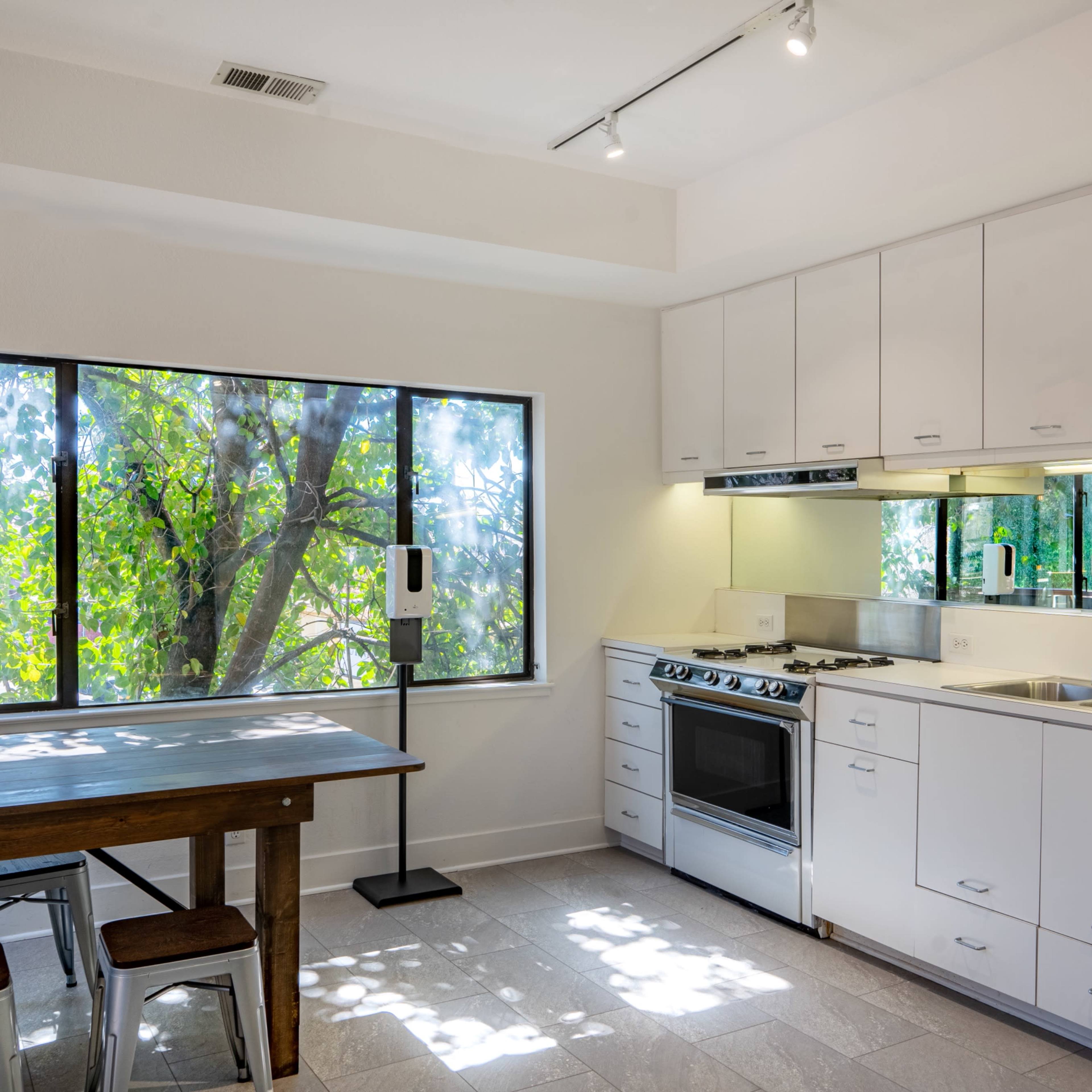 The kitchen features white cabinetry, stainless steel appliances, and a dining area beside a large window overlooking greenery.