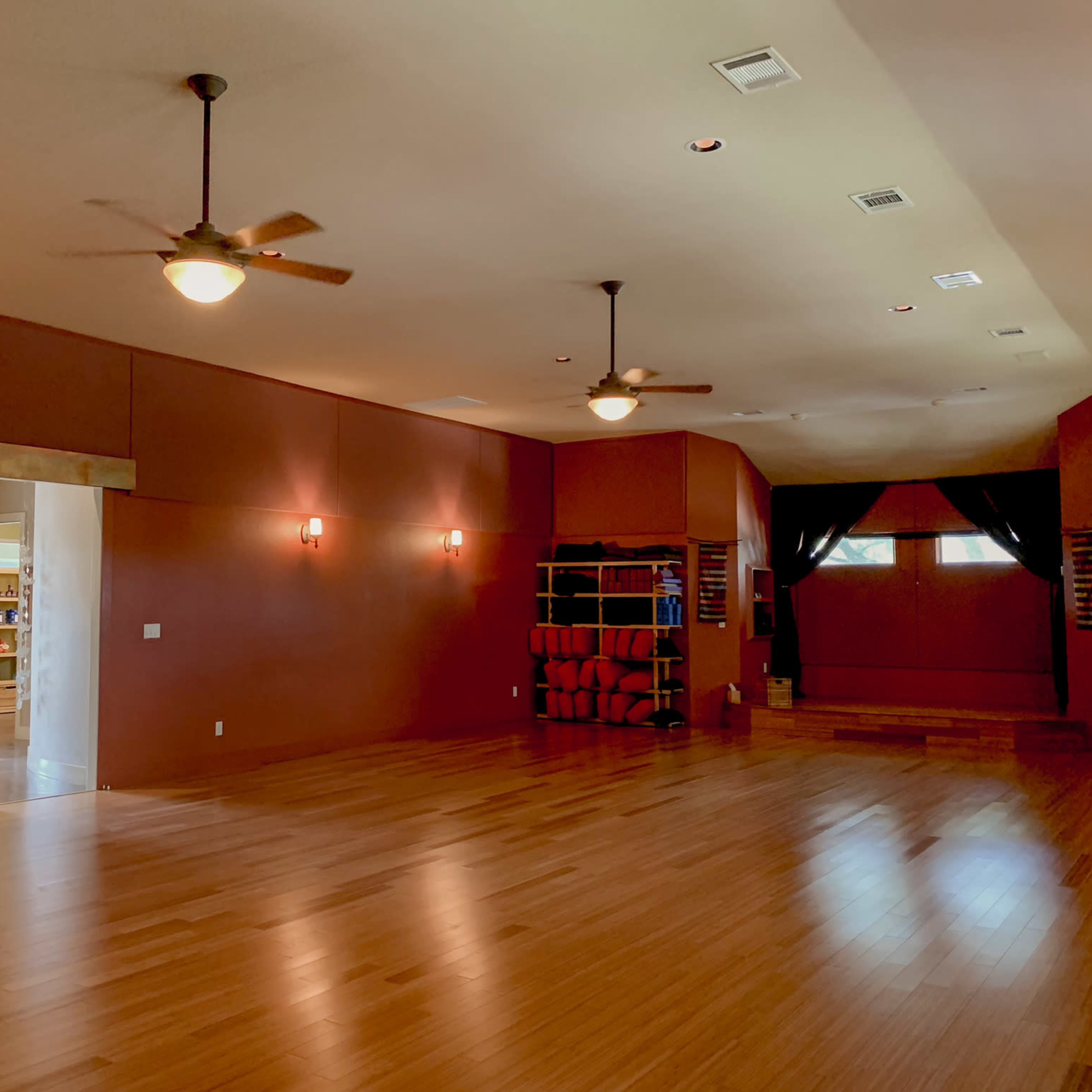 An empty yoga studio with wooden floors, soft lighting, and a doorway leading to another room.