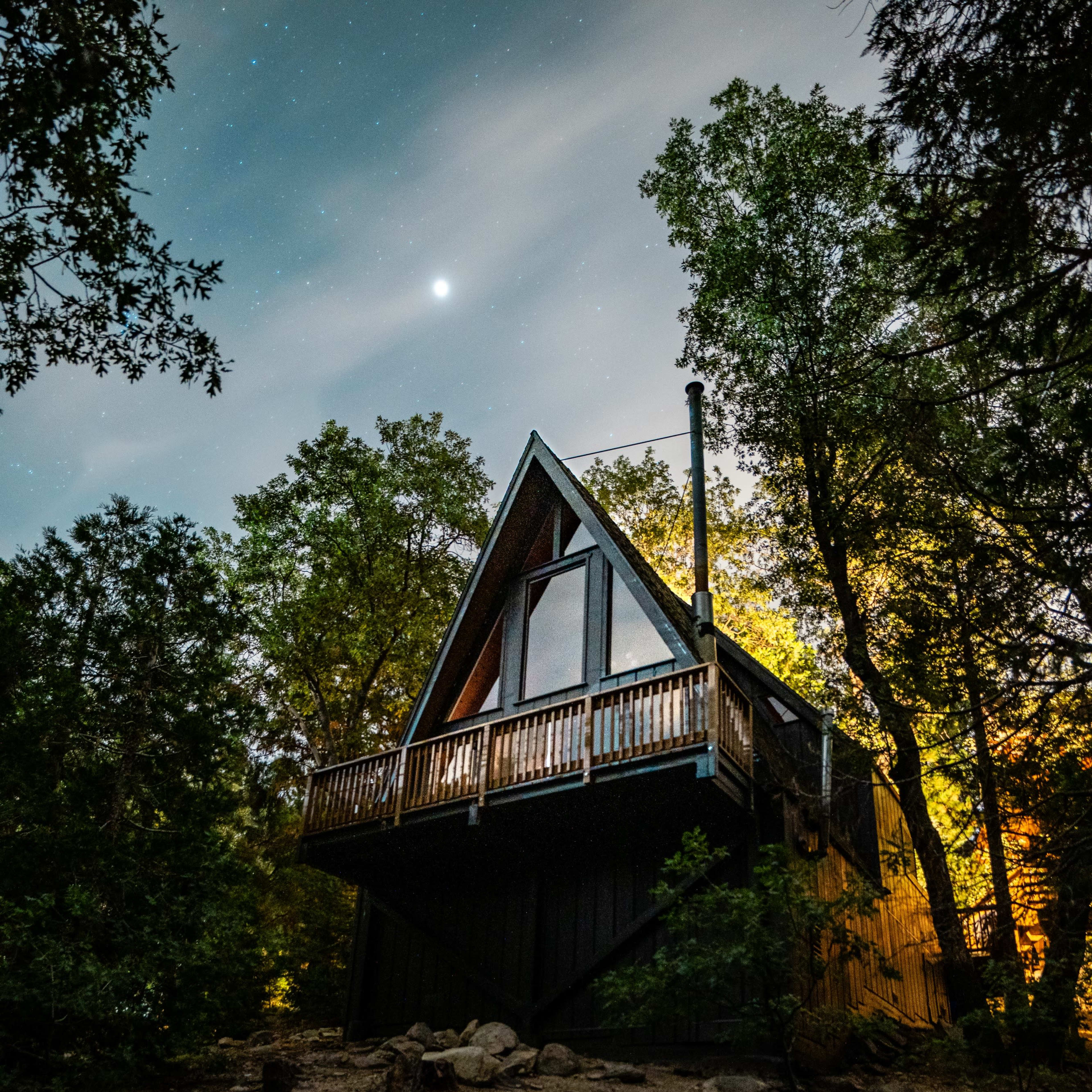 A modern A-frame cabin is elevated on stilts surrounded by trees under a starry night sky.