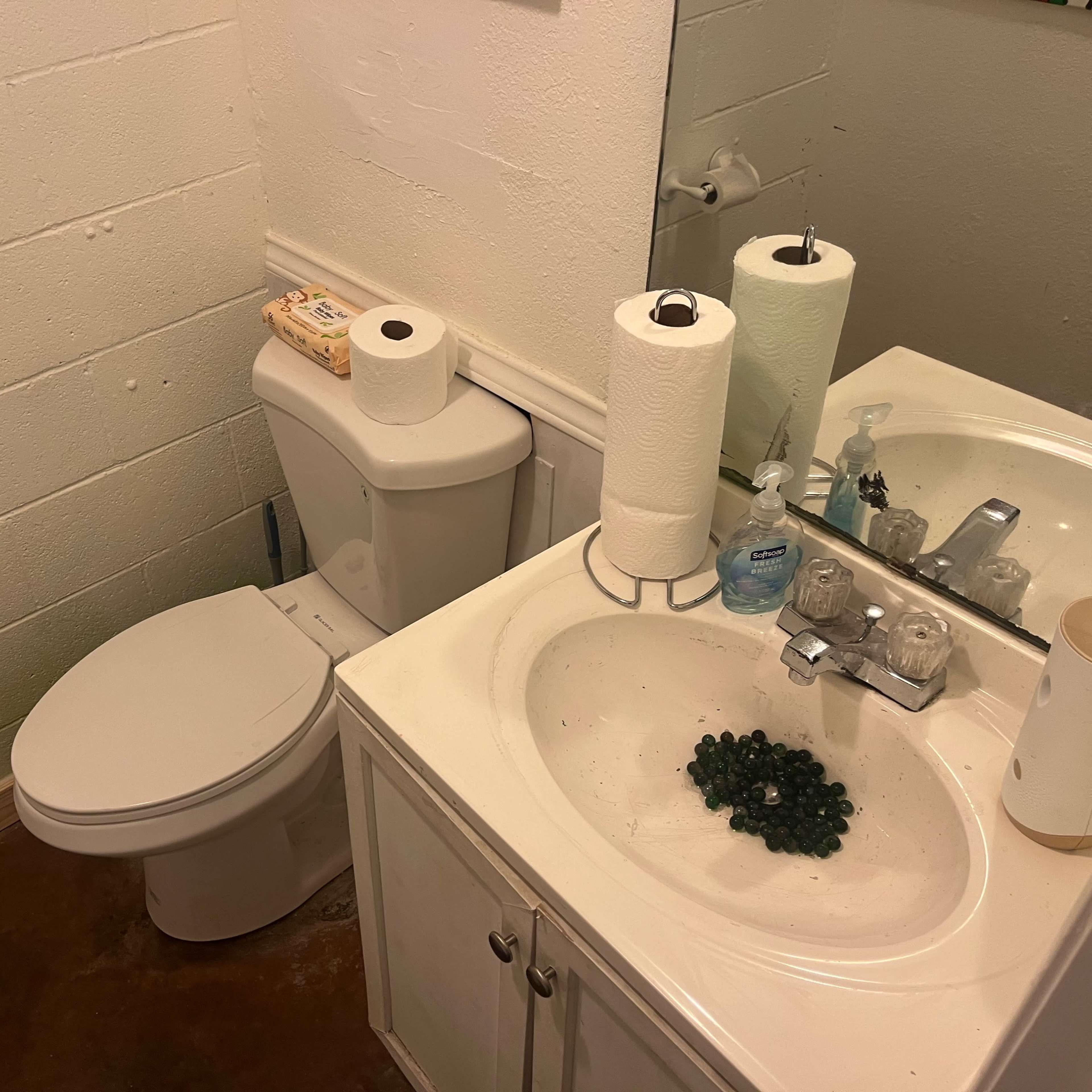 A small bathroom with a toilet, a sink, and various bathroom items, including paper towels and a plate of grapes on the countertop.