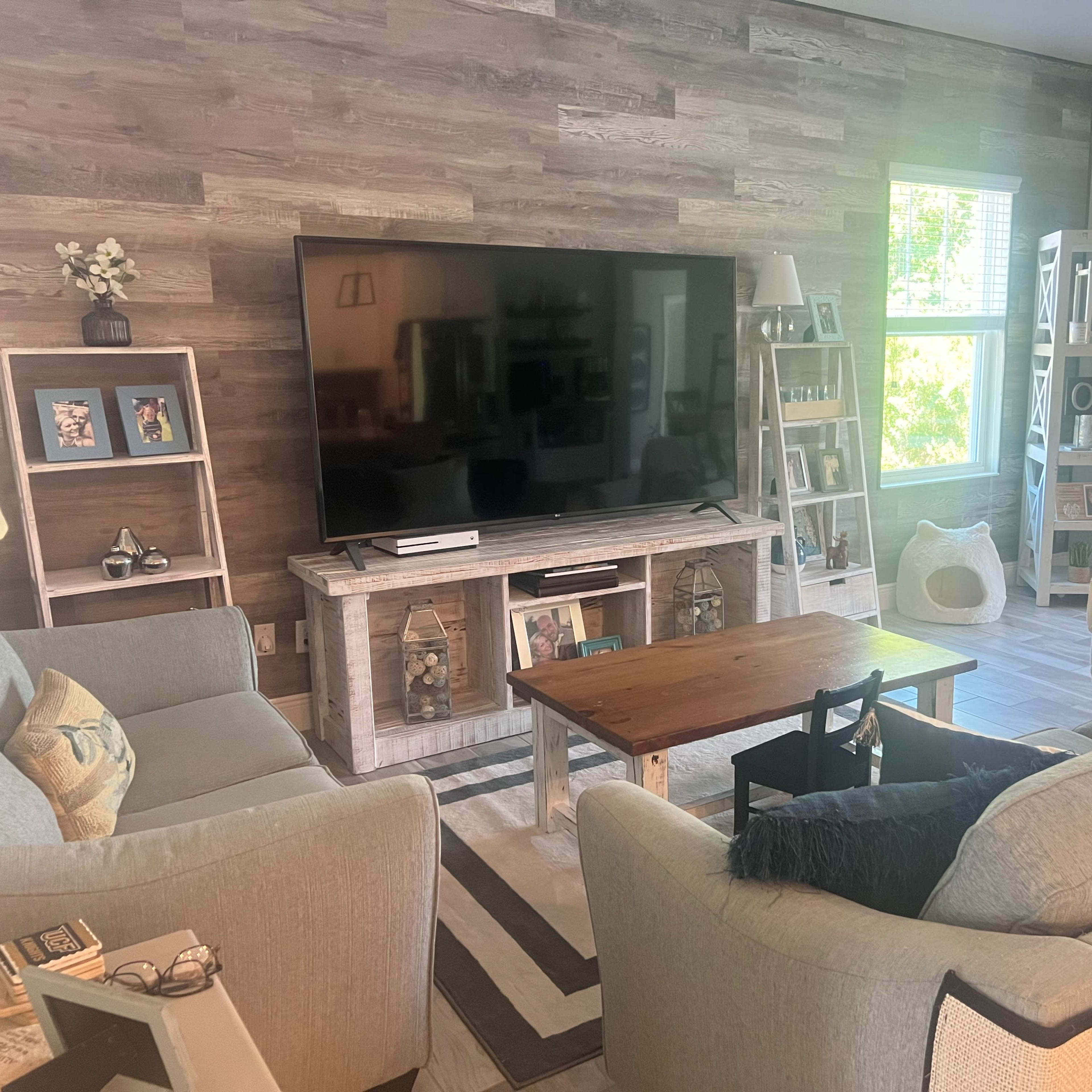 The living room features a large television mounted on a wooden wall with a coffee table in front of a sectional sofa and armchairs arranged around it.
