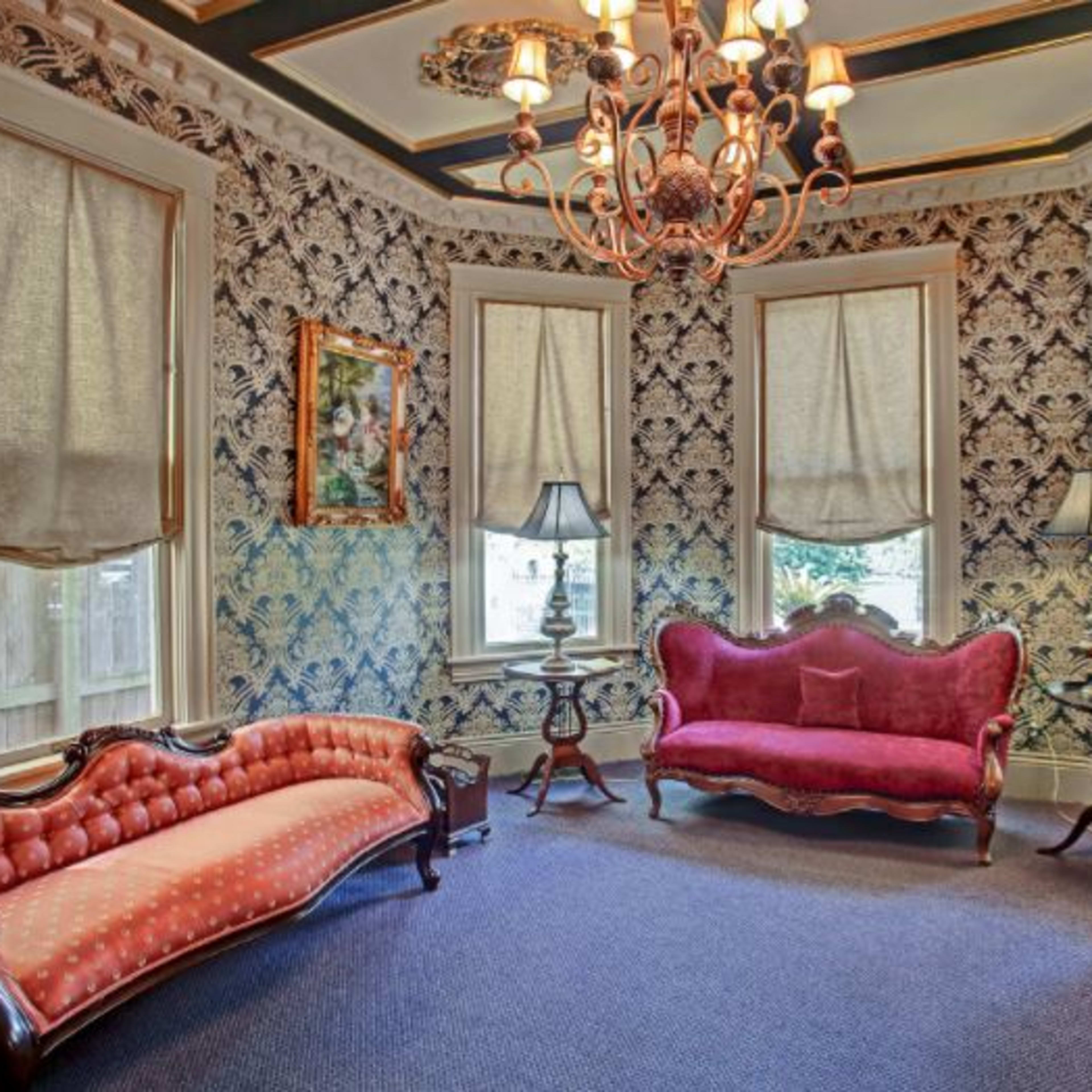 The room features vintage furniture, including two sofas and a chair, set against patterned wallpaper and illuminated by a chandelier.