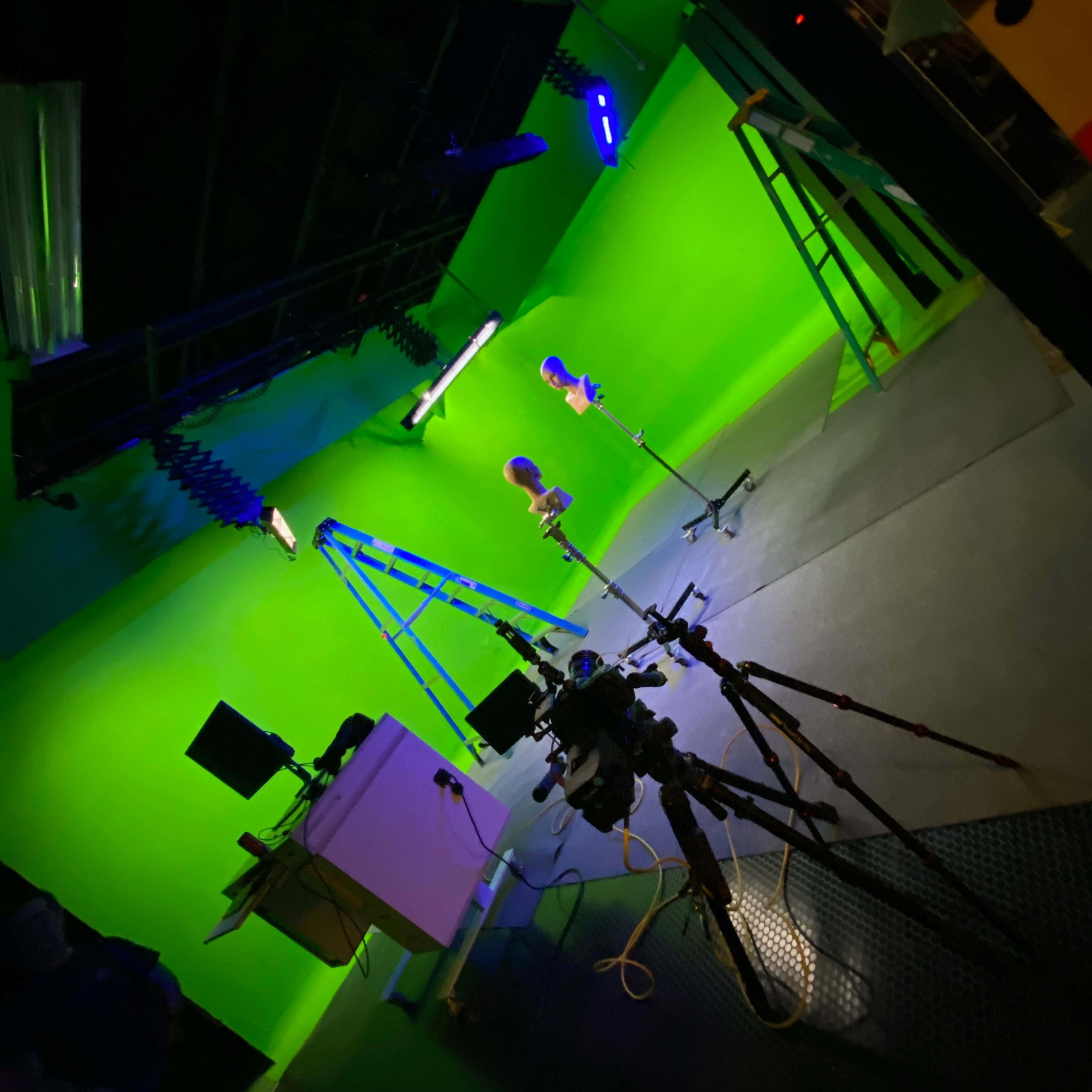 A green screen studio setup with two microphones on stands, a camera on a tripod, and lighting equipment.