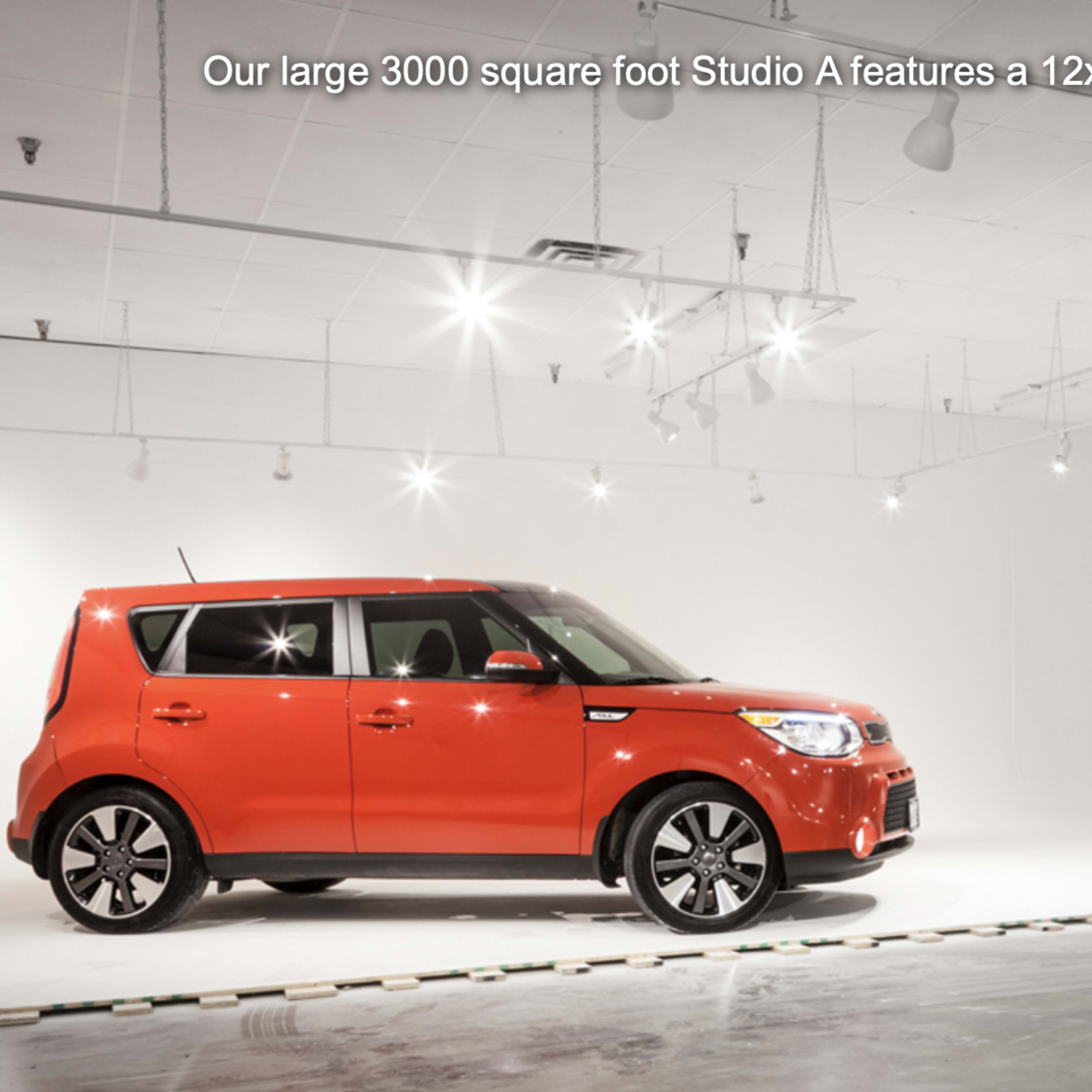 A red car is positioned in a well-lit, spacious studio with white walls and a cyclorama backdrop.
