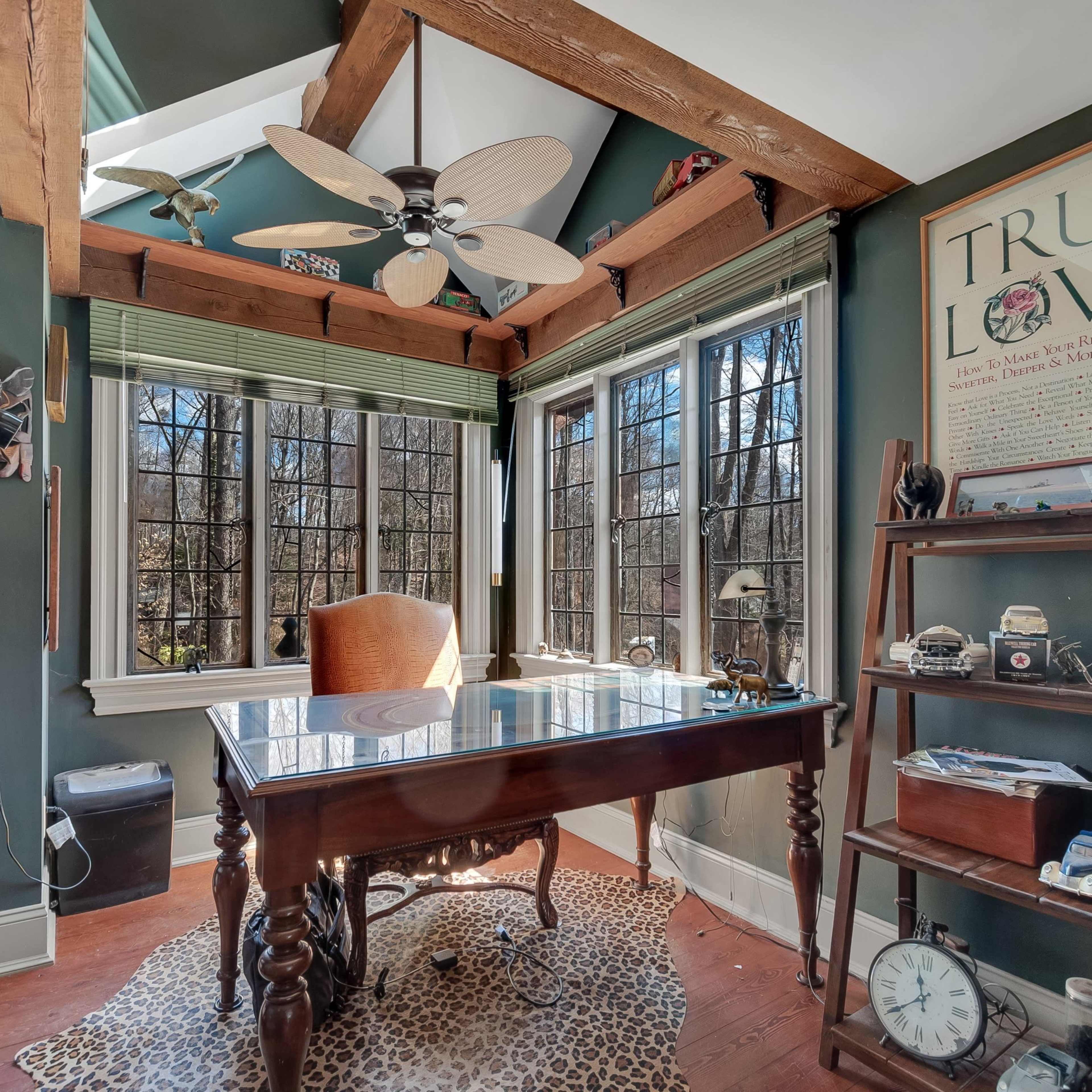 A home office features a wooden desk, large windows with green shades, and decorative elements including an elephant statue and a vintage camera collection.