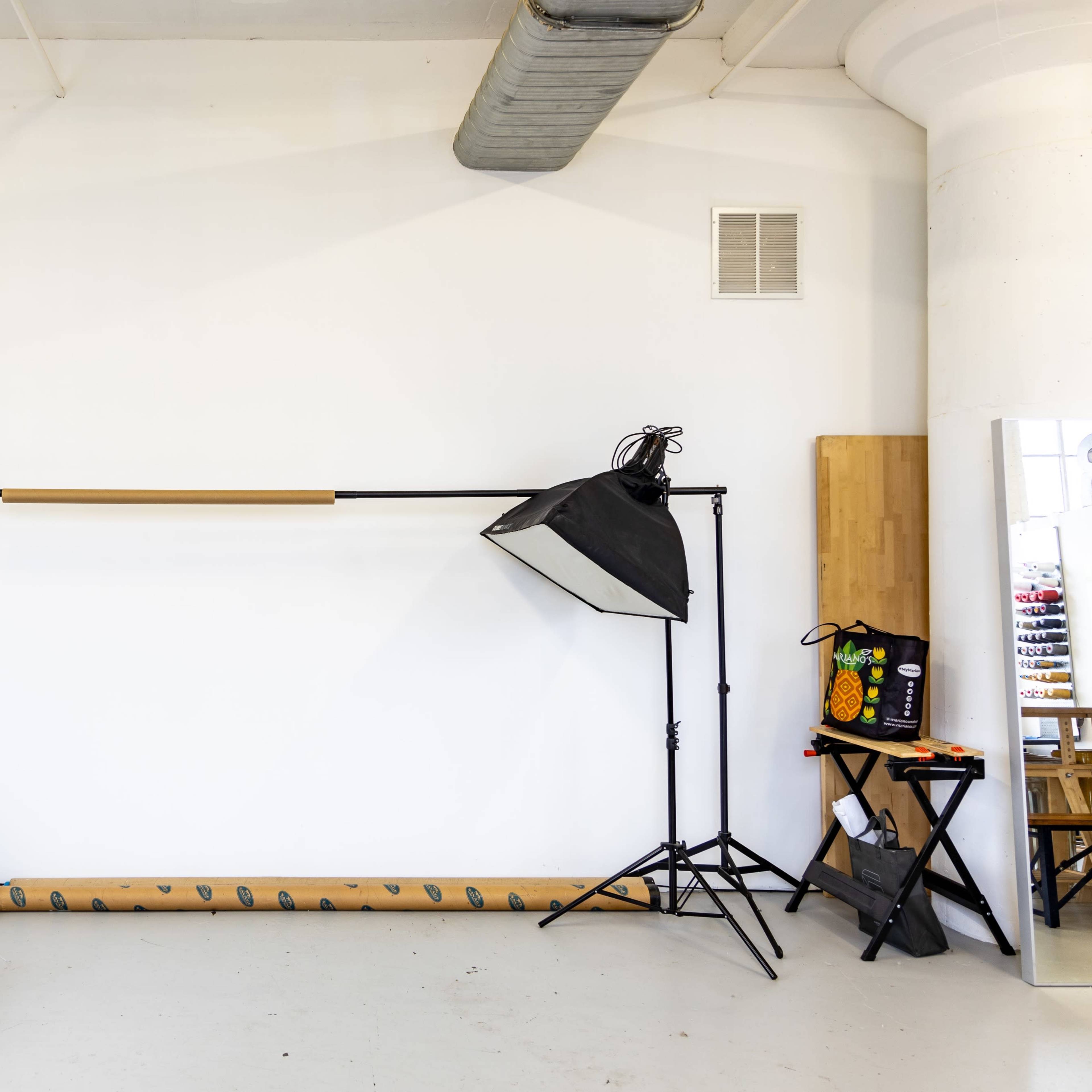 A minimalistic studio space features a gray couch, a lighting setup on a stand, and a vertical mirror against a white wall.