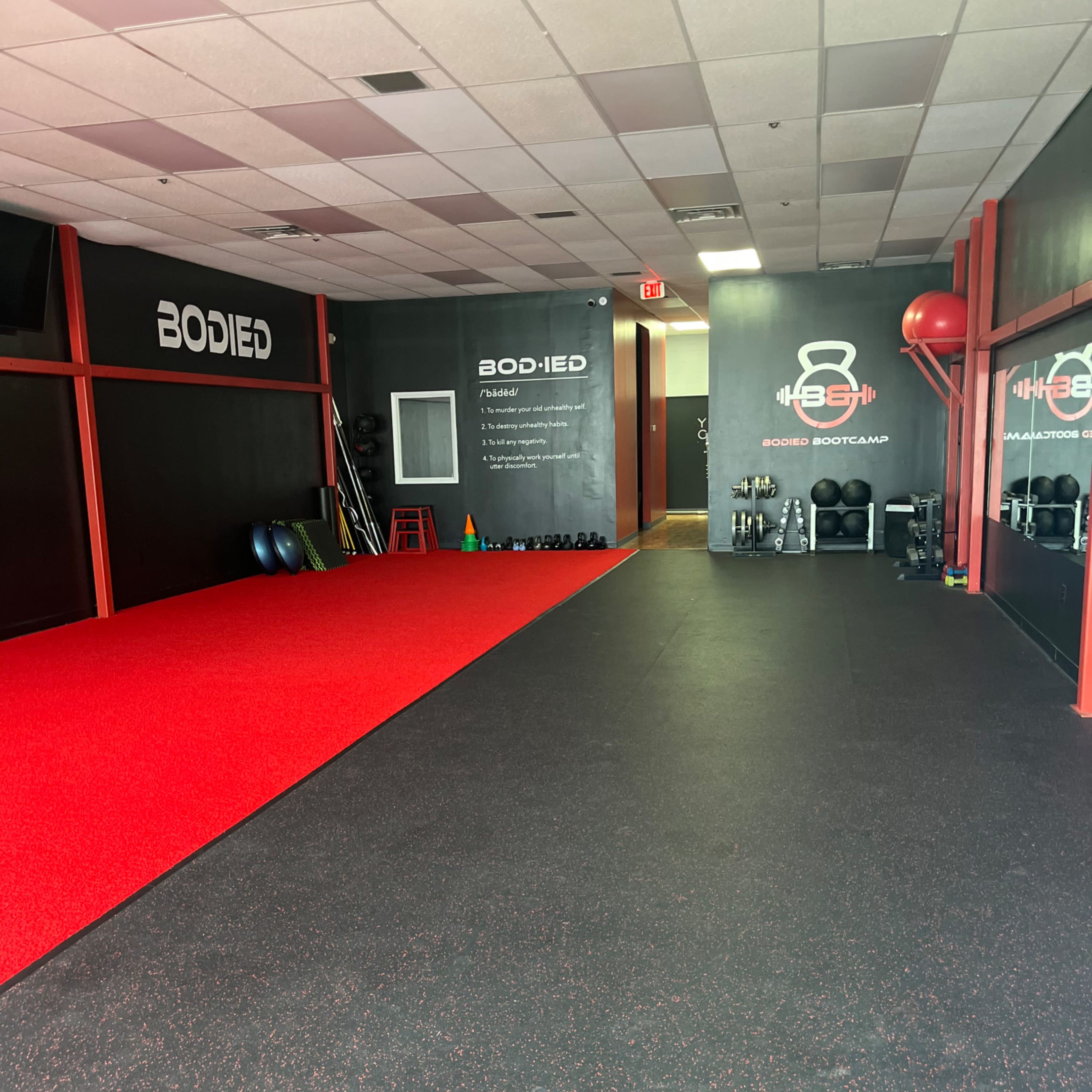 A fitness studio with red and black rubber flooring, equipped with various workout equipment along the walls.
