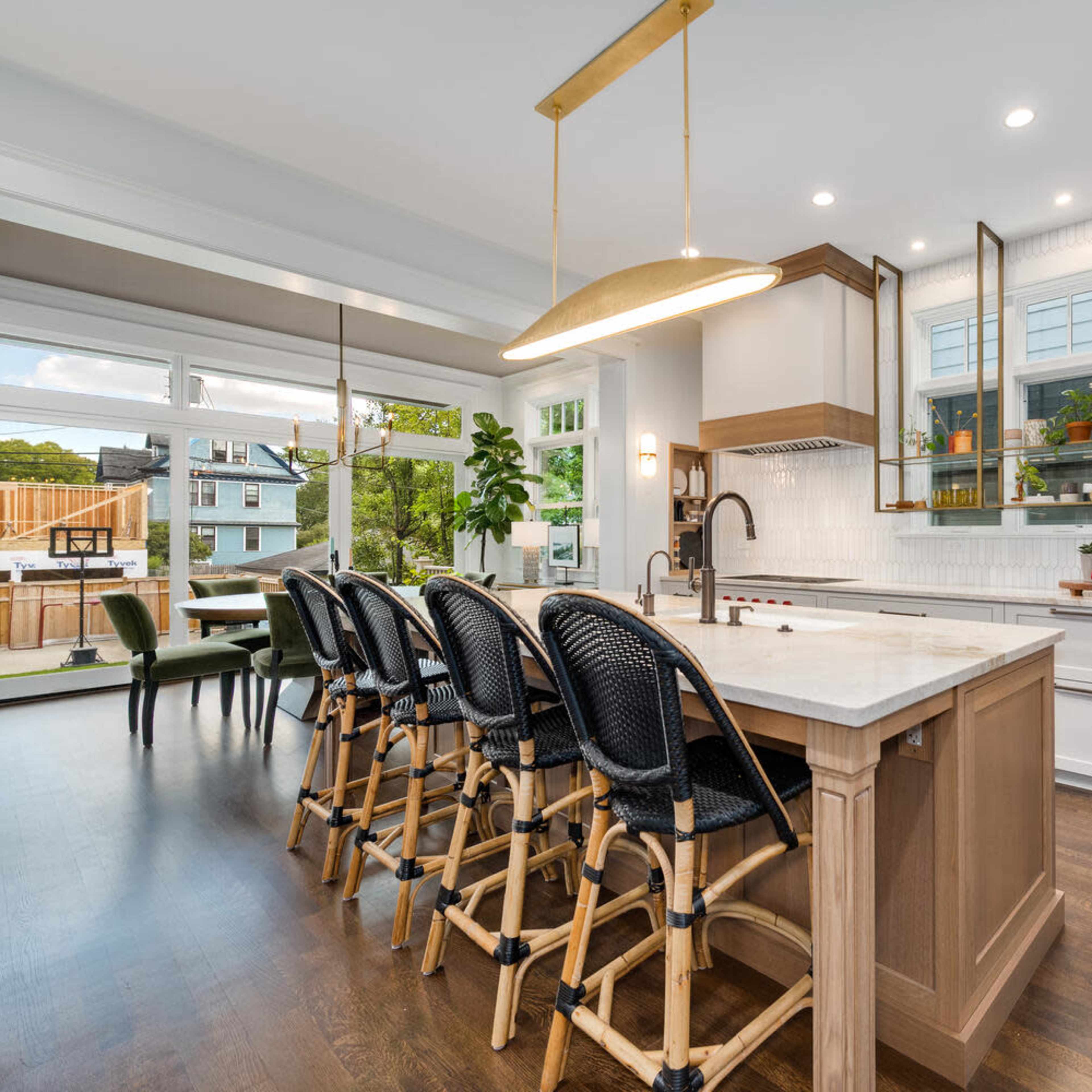 A modern kitchen featuring a large island with bar stools, white cabinetry, and large windows providing natural light.
