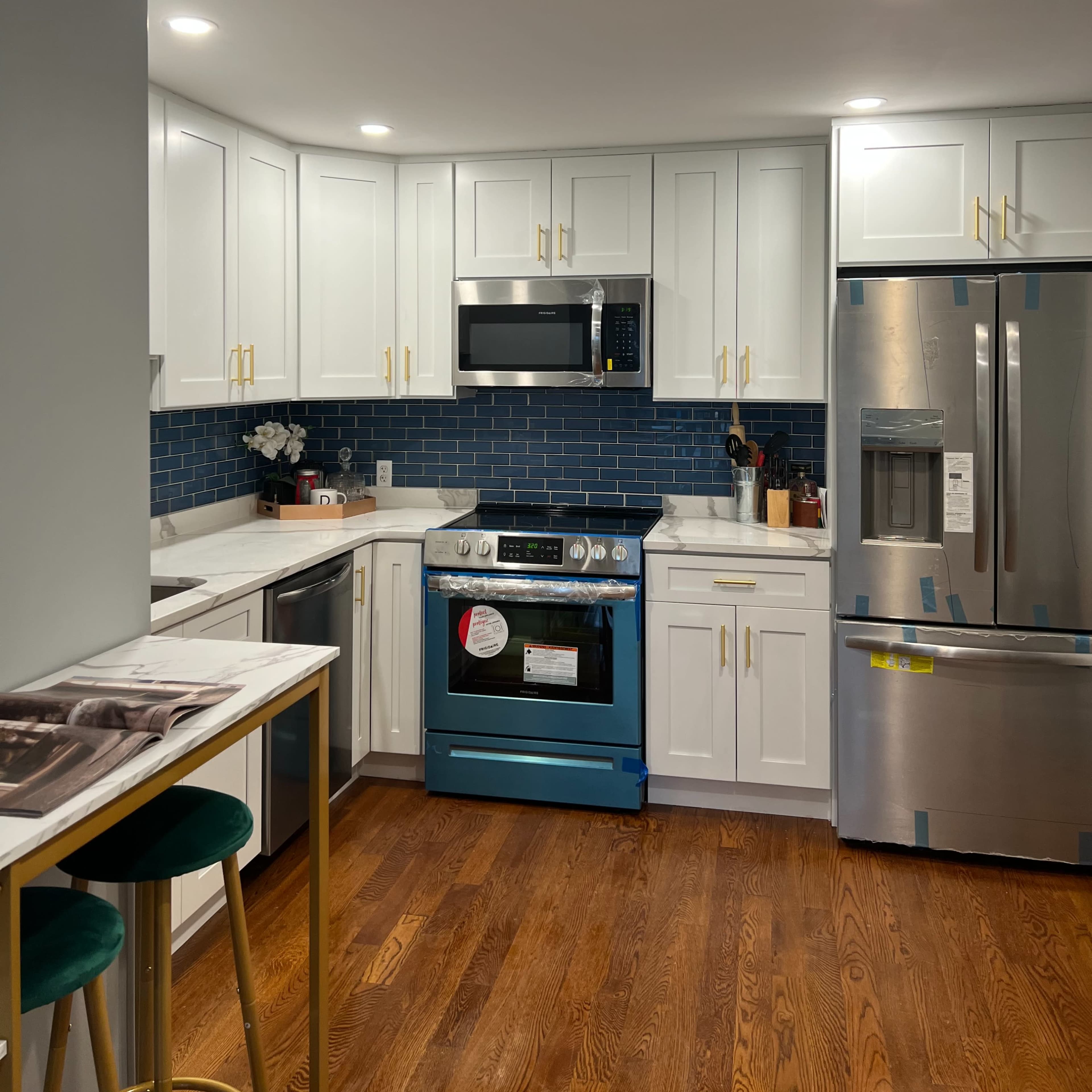 A modern kitchen with white cabinets, a blue tile backsplash, stainless steel appliances, and wooden flooring.