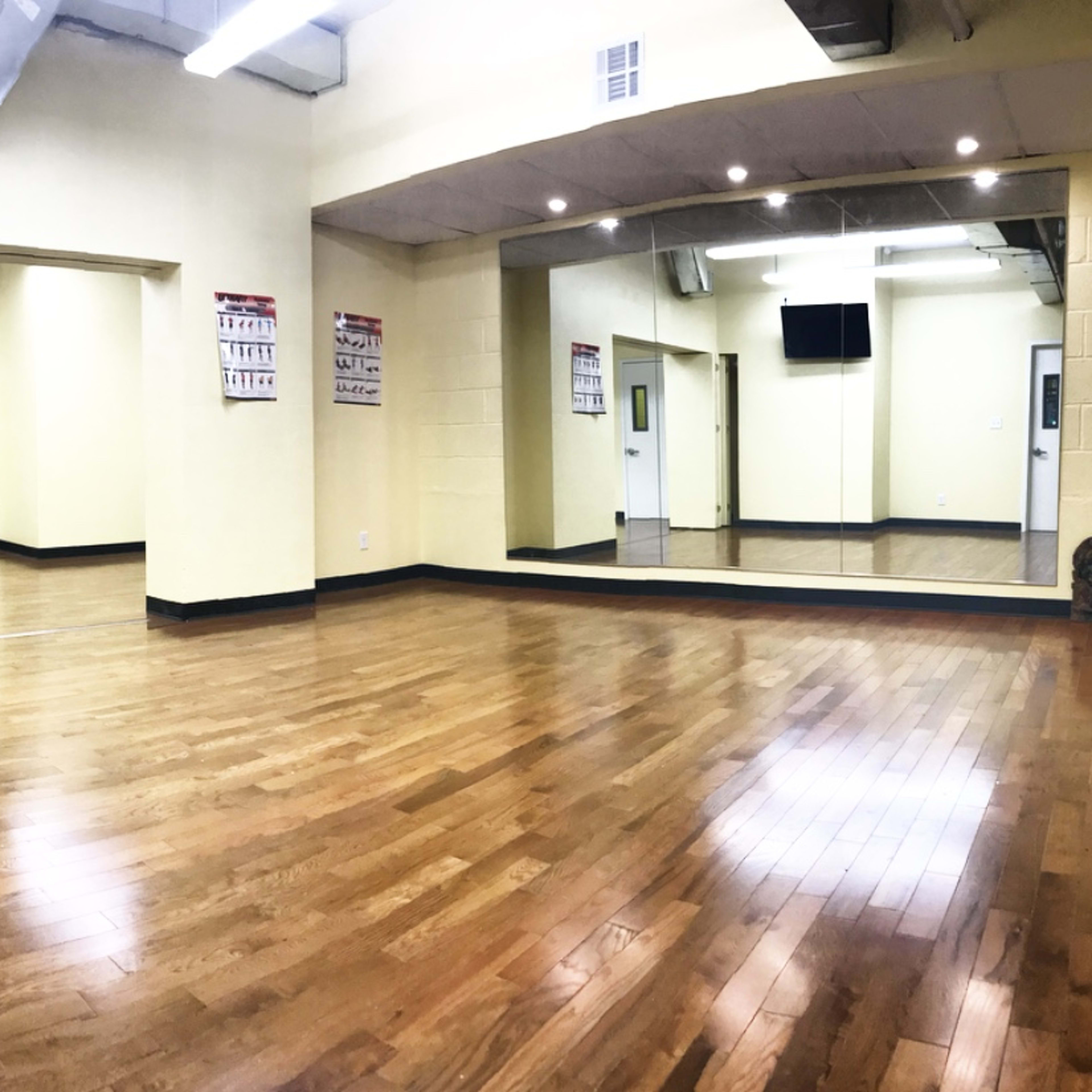A spacious, empty room with yellow walls, wooden flooring, and a large mirror along one wall.