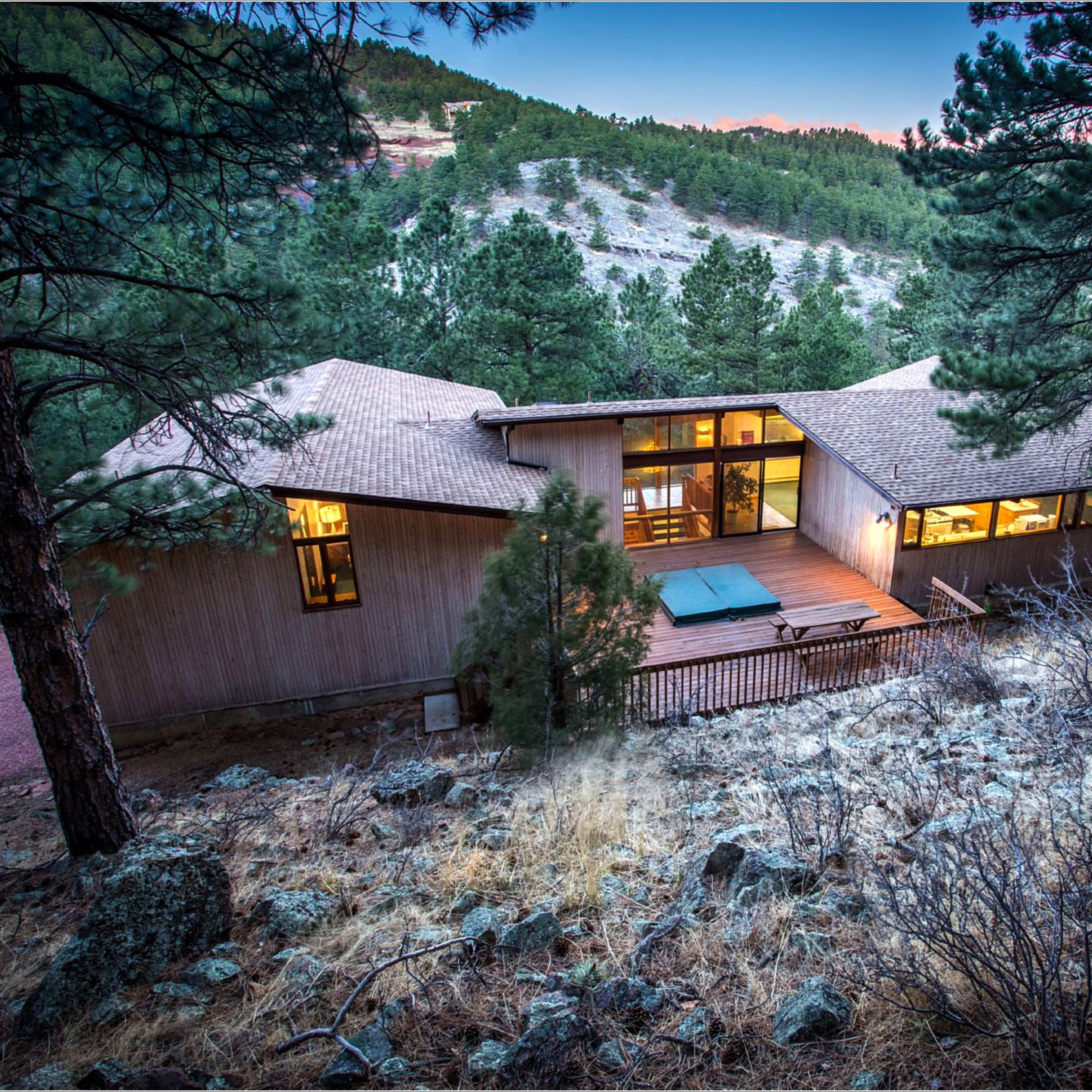 A modern house is situated on a hillside surrounded by trees and rocky terrain.