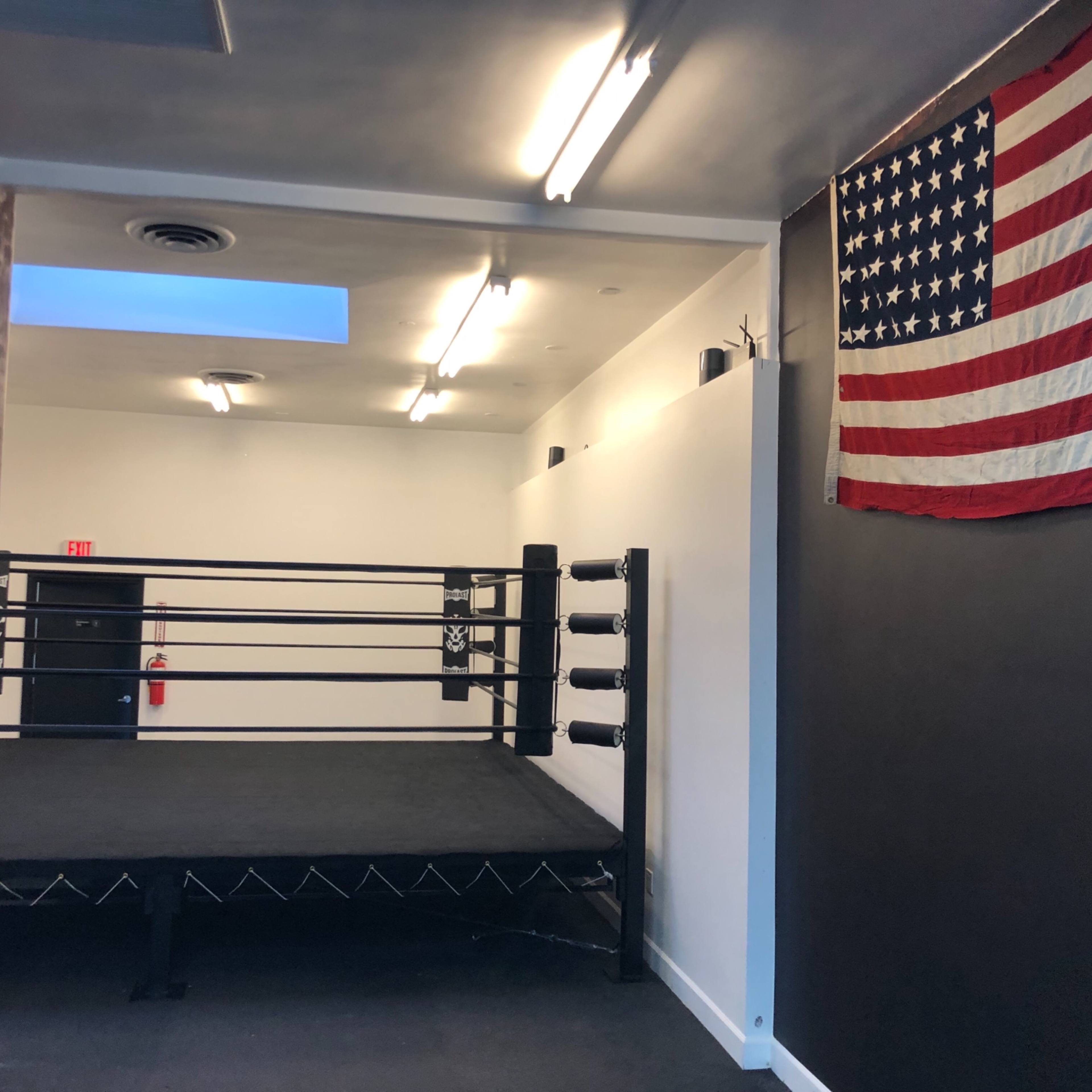 A boxing ring set up in a minimalist room with an American flag mounted on the wall.