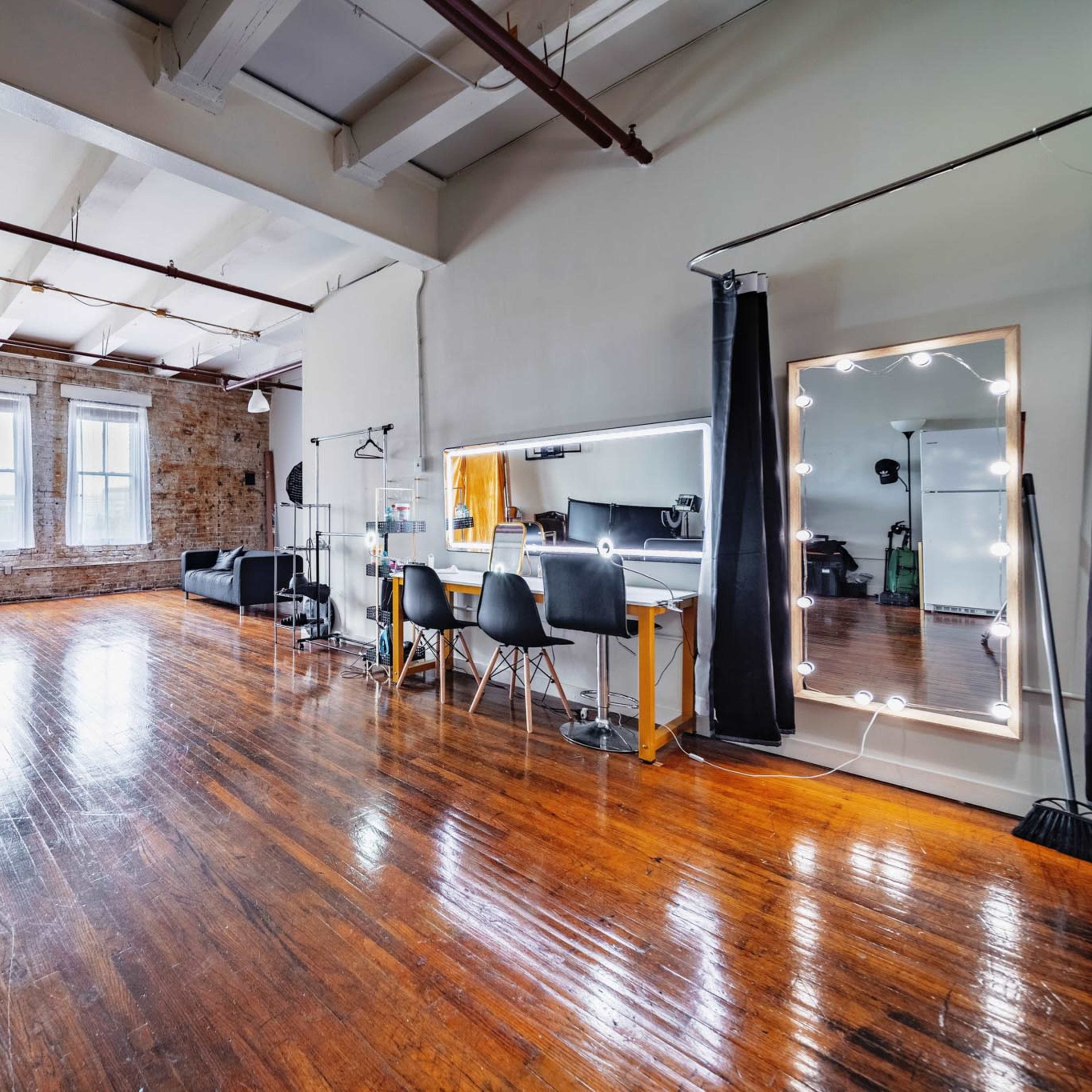 A spacious studio features hardwood floors, large windows, and a small area with a mirror and chairs for activities.